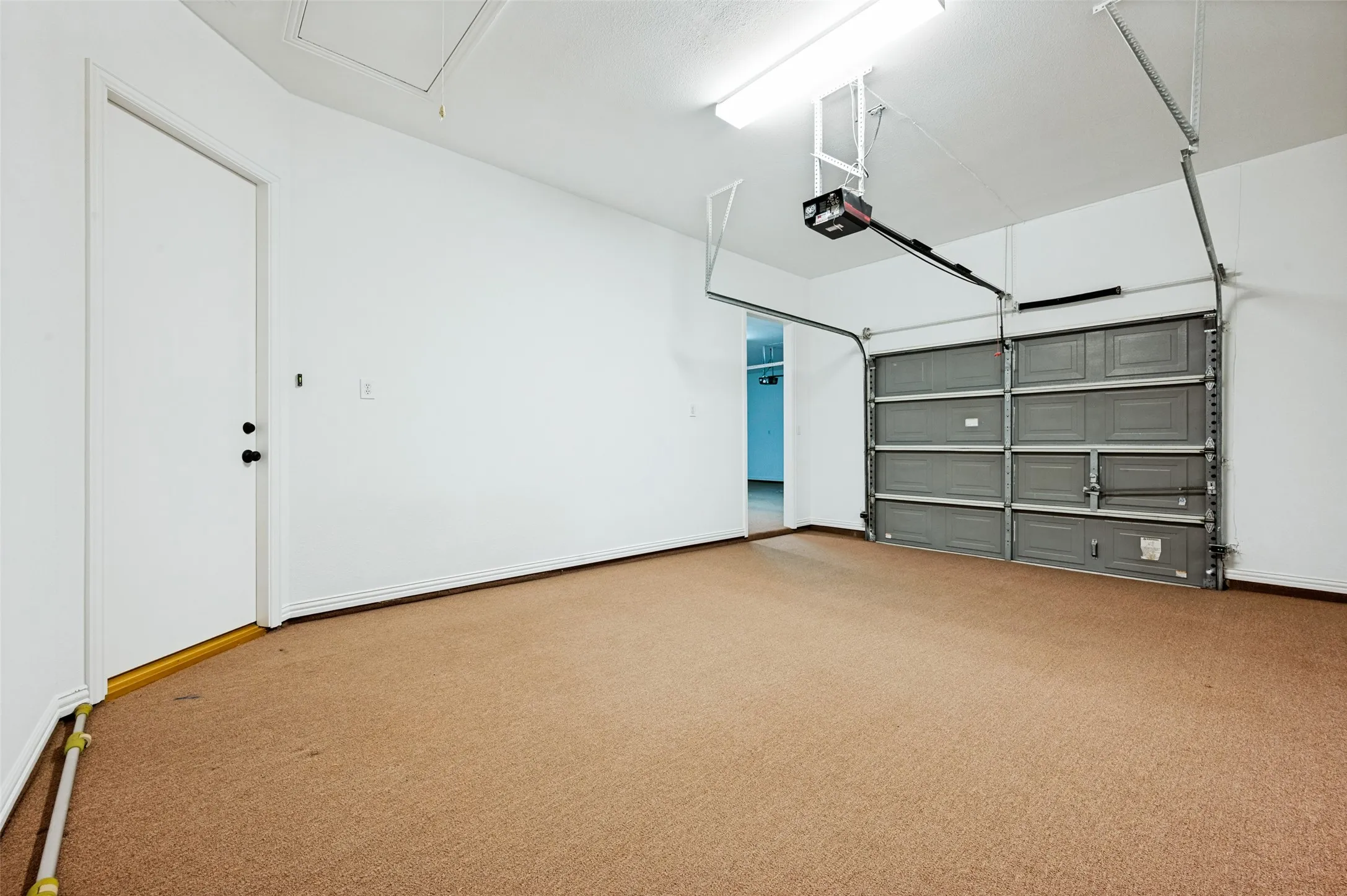 Two-car garage featuring a tan carpeted floor, white walls, and a grey paneled garage door