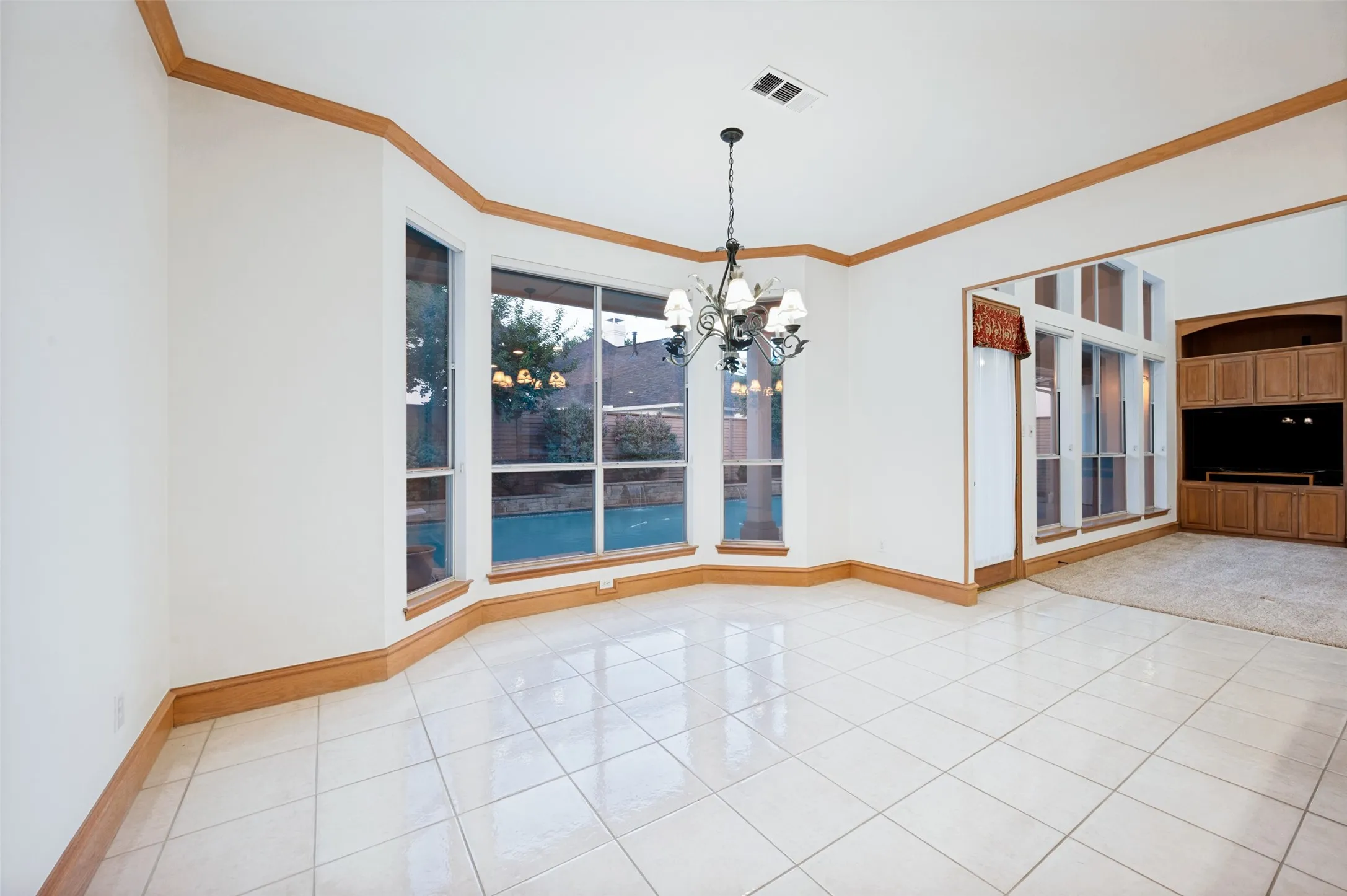 Spacious room featuring large bay windows, a multi-bulb chandelier, and light tile flooring