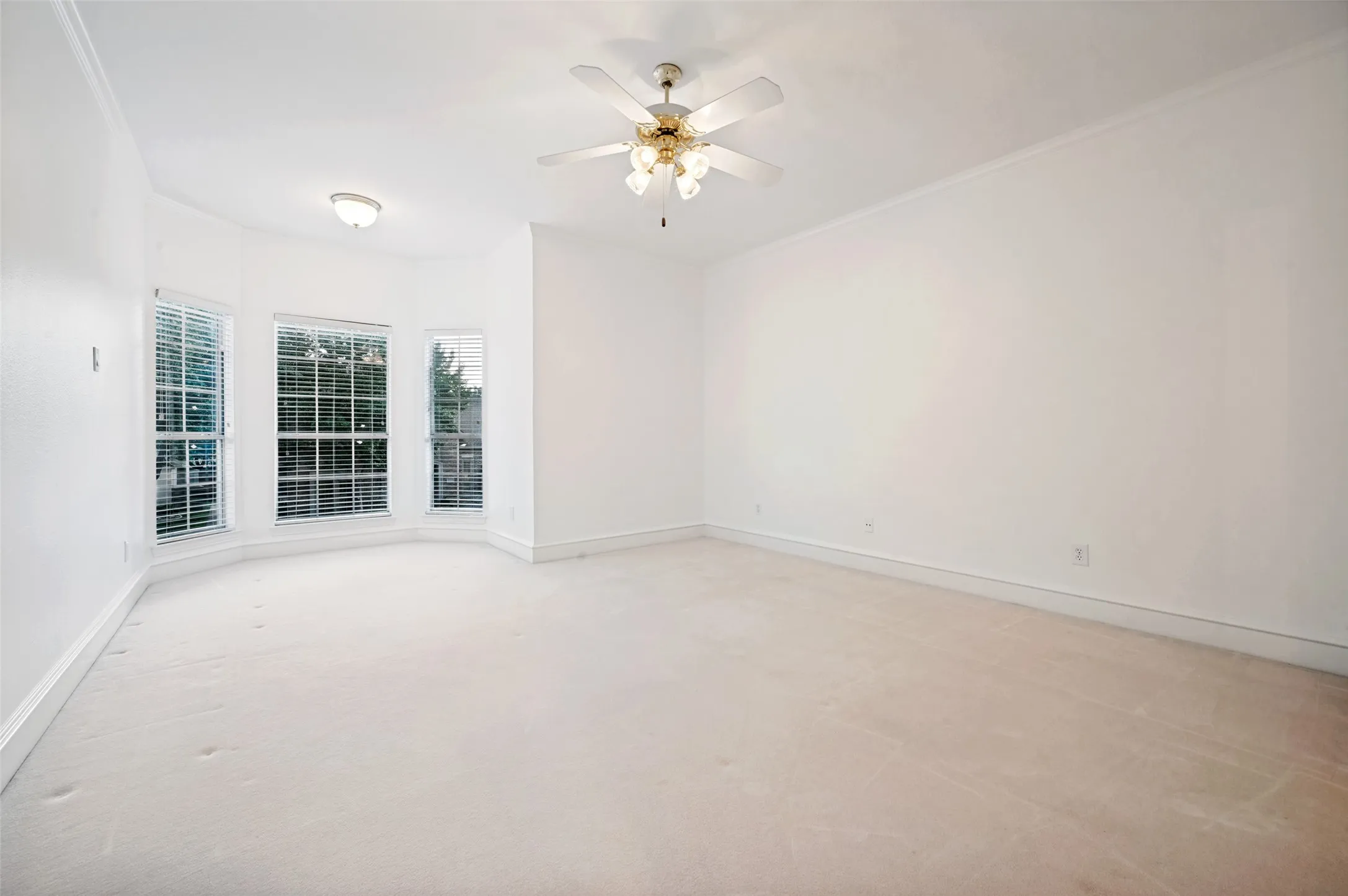 Spacious room featuring a bay window with multiple paneled windows, light-toned carpeting, and a ceiling fan with integrated lighting