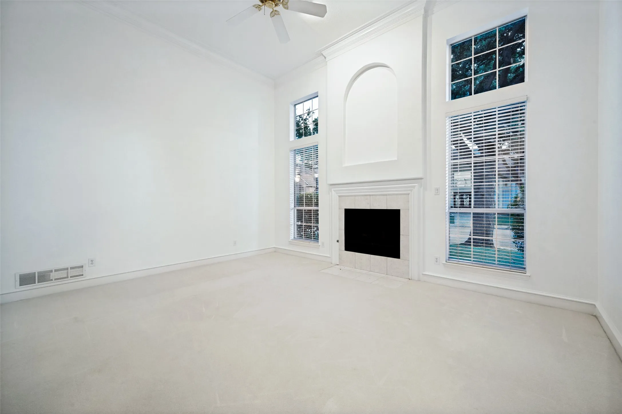 Vaulted ceilings featuring a ceiling fan, a fireplace with a mantel and tile surround, and tall windows with blinds