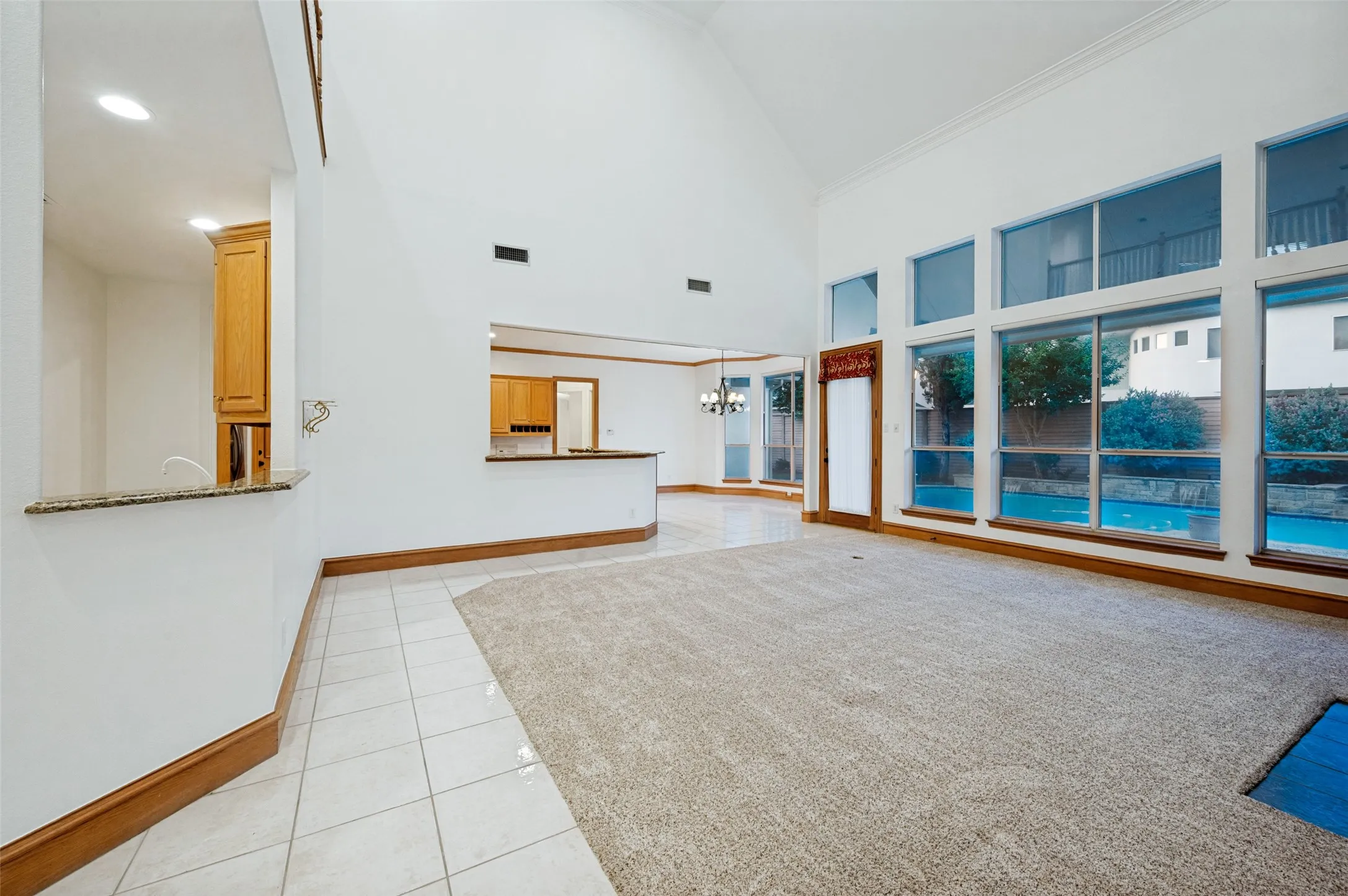 Spacious living area featuring a vaulted ceiling, extensive window wall, and light-toned carpet flooring