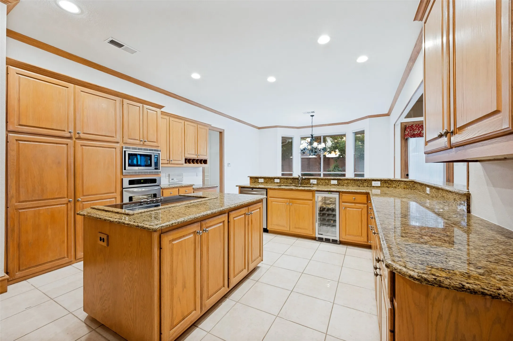 Kitchen featuring a central island with a built-in cooktop, granite countertops, extensive cabinetry, integrated wall oven and microwave, and a beverage cooler