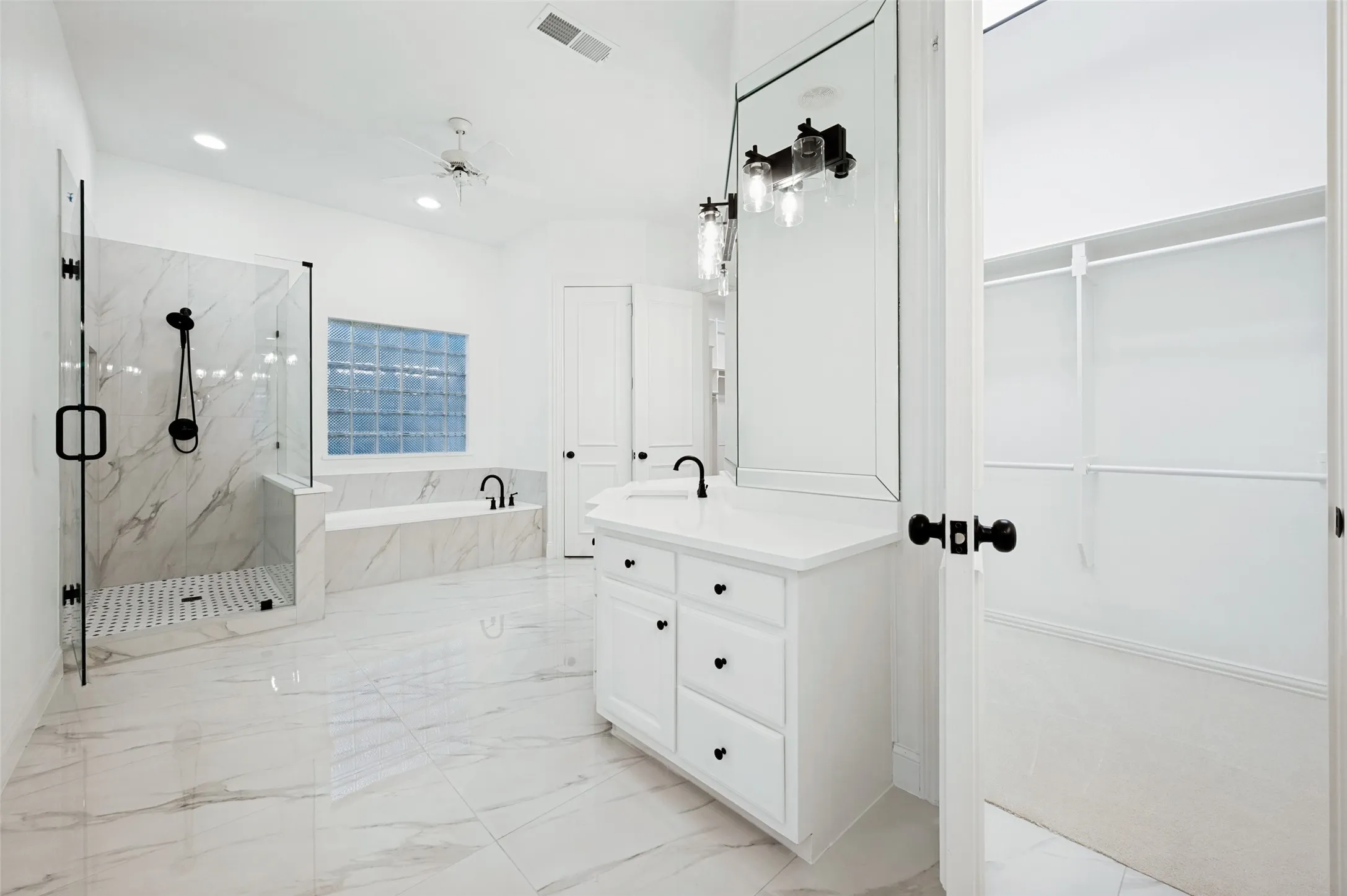 Primary bathroom featuring large format marble-look tile flooring, a glass-enclosed shower with black fixtures, and a soaking tub with a glass block window