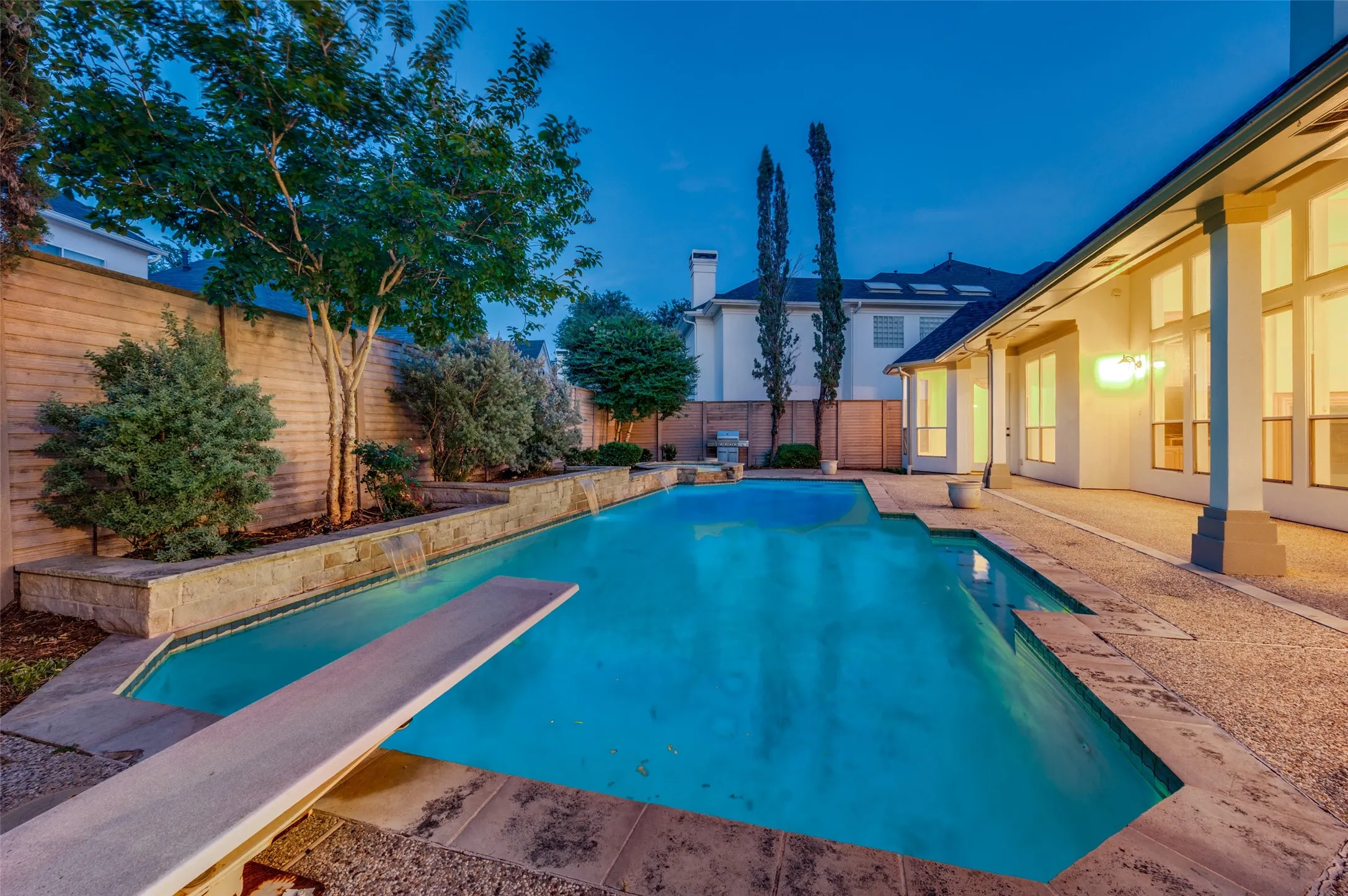 Outdoor swimming pool with a diving board, surrounded by stone coping and an exposed aggregate patio