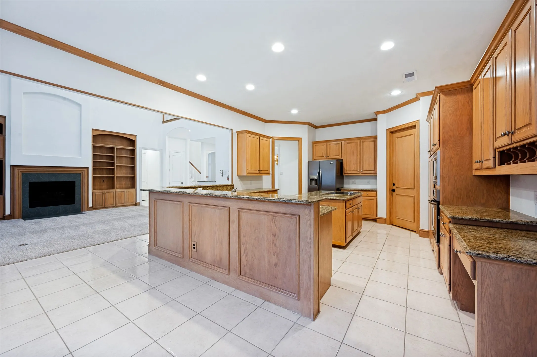 Kitchen featuring light wood cabinetry, granite countertops, an island with paneling, and tile flooring