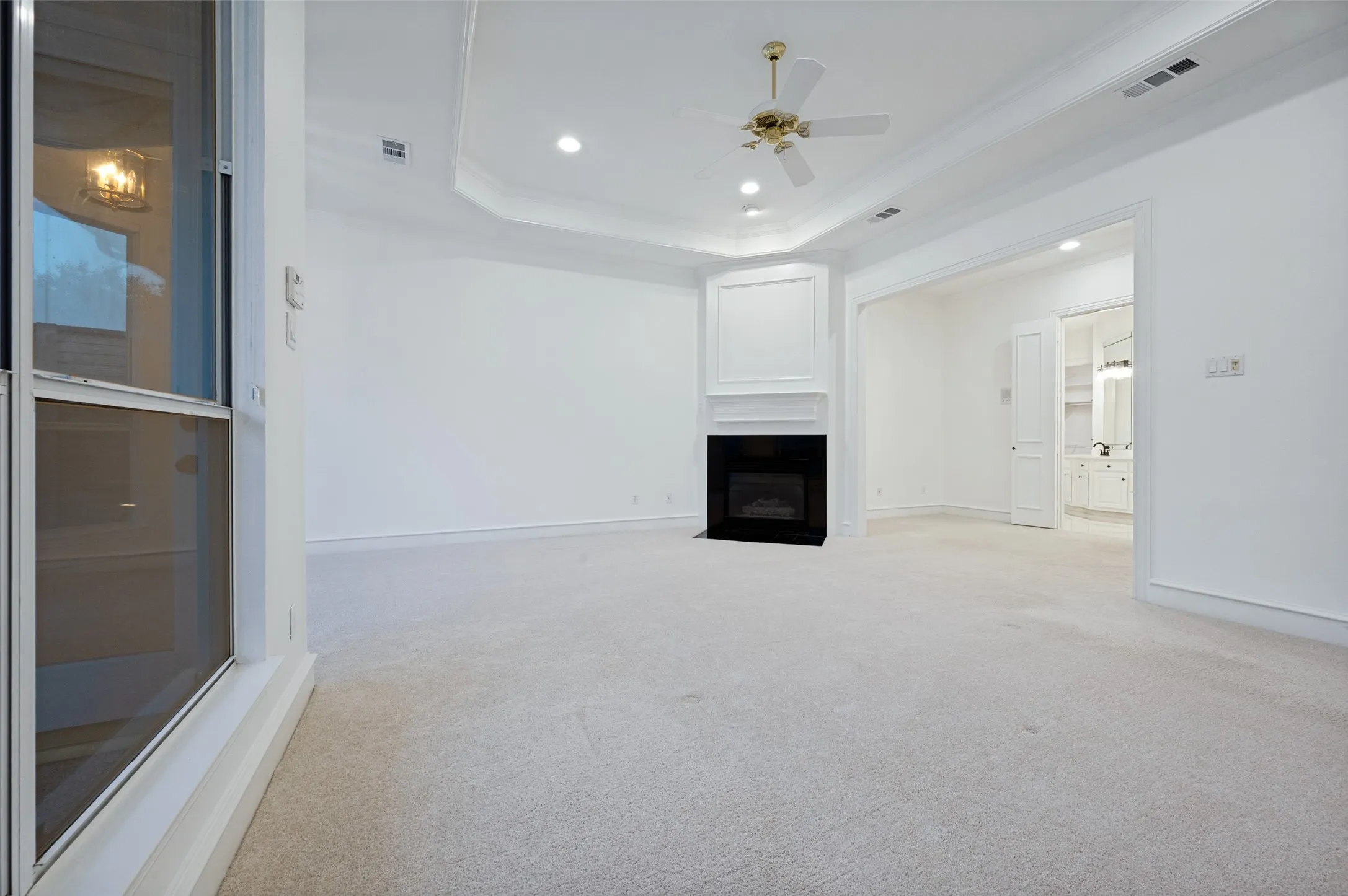 Spacious room featuring a corner fireplace with decorative molding, tray ceiling, recessed lighting, and a ceiling fan