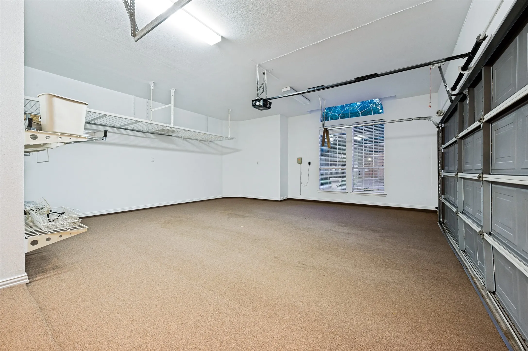 Spacious garage featuring a light brown carpeted floor, overhead fluorescent lighting, and a large multi-pane window