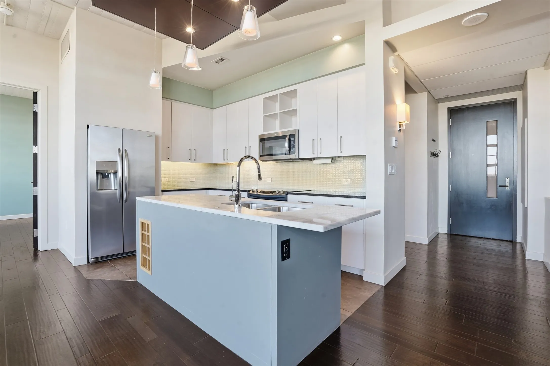 Kitchen featuring an expansive island with a light blue finish, stainless steel appliances, white cabinetry, undermount sink, and dark wood-finish flooring