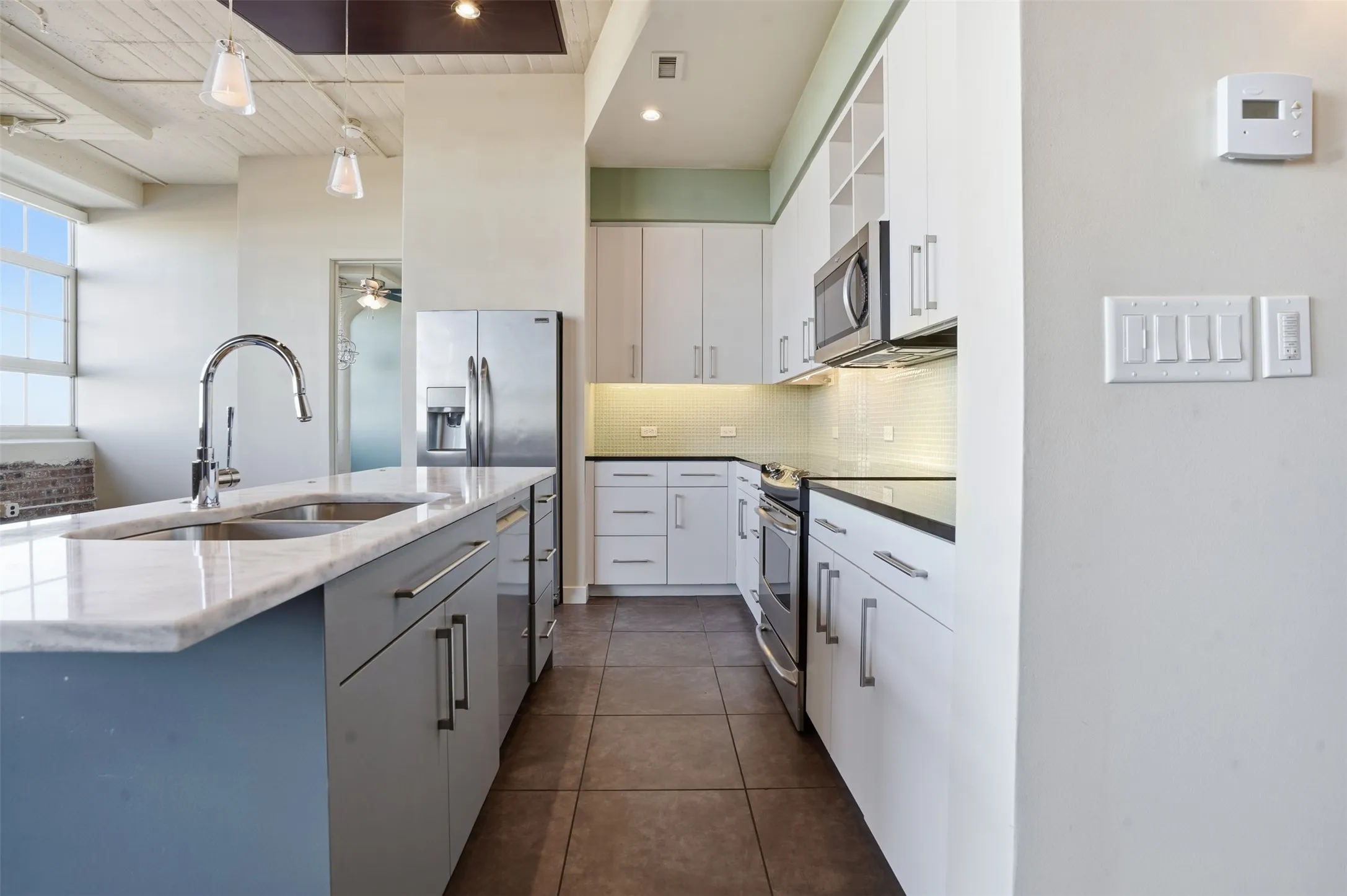 Modern kitchen featuring a large island with an undermount sink and chrome faucet, stainless steel appliances, white cabinetry, dark countertops, and tile flooring