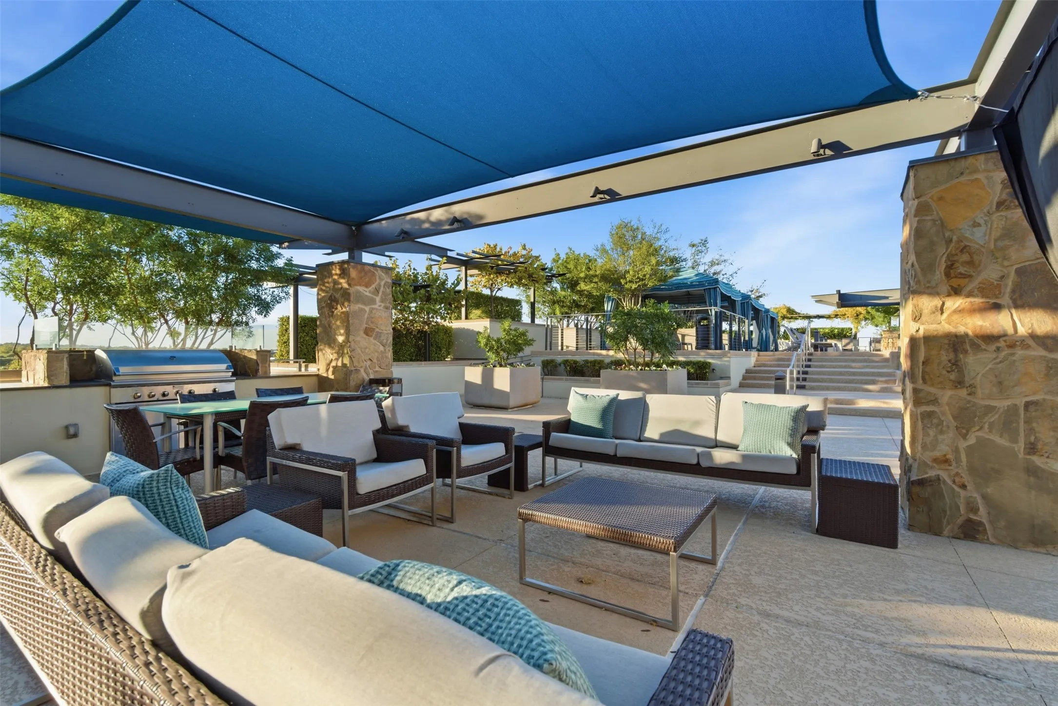 Outdoor living area featuring a blue shade canopy, integrated stone columns, and an outdoor kitchen with a built-in grill