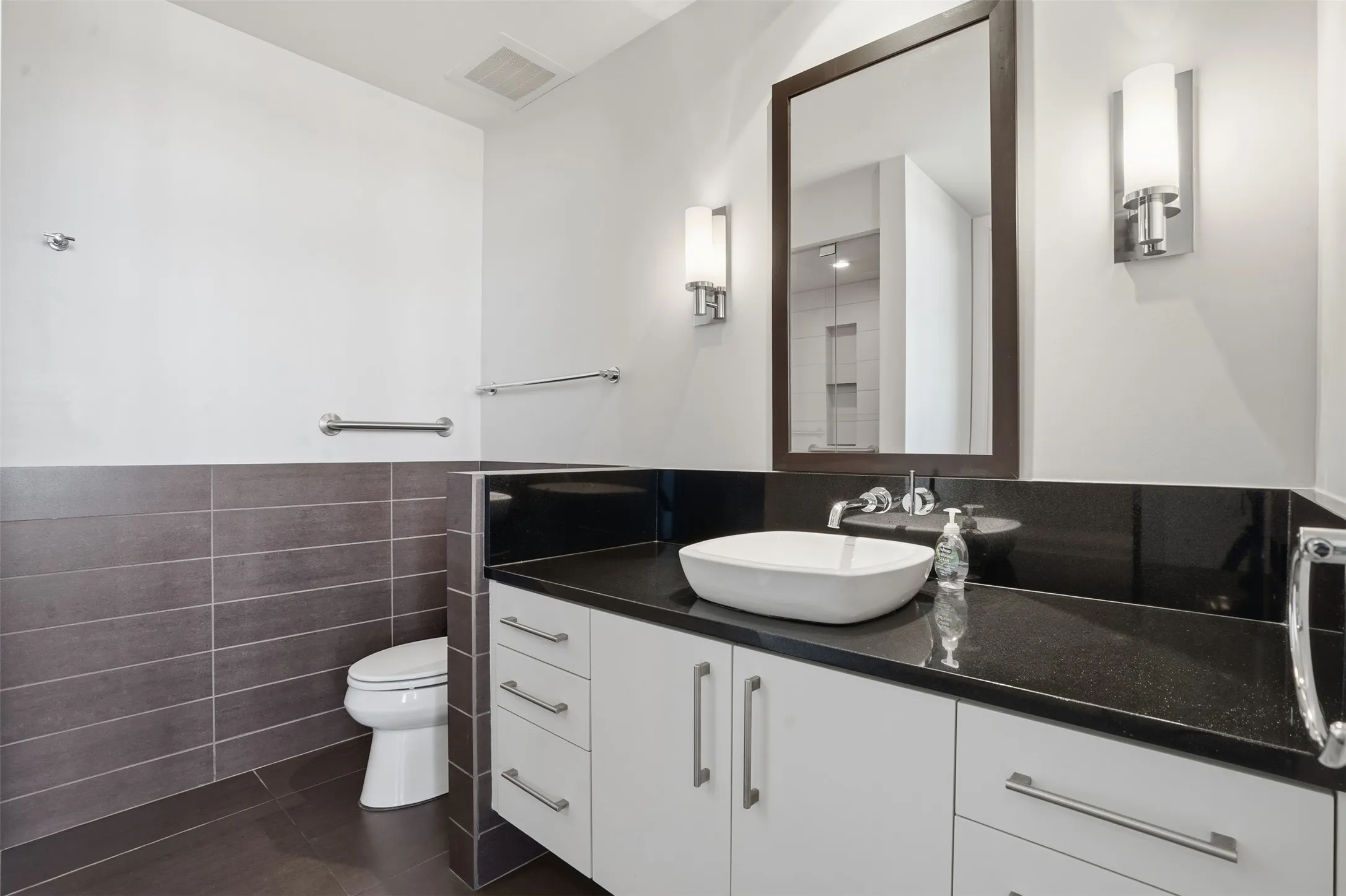 Modern vanity featuring a vessel sink, dark stone countertop, and white cabinetry