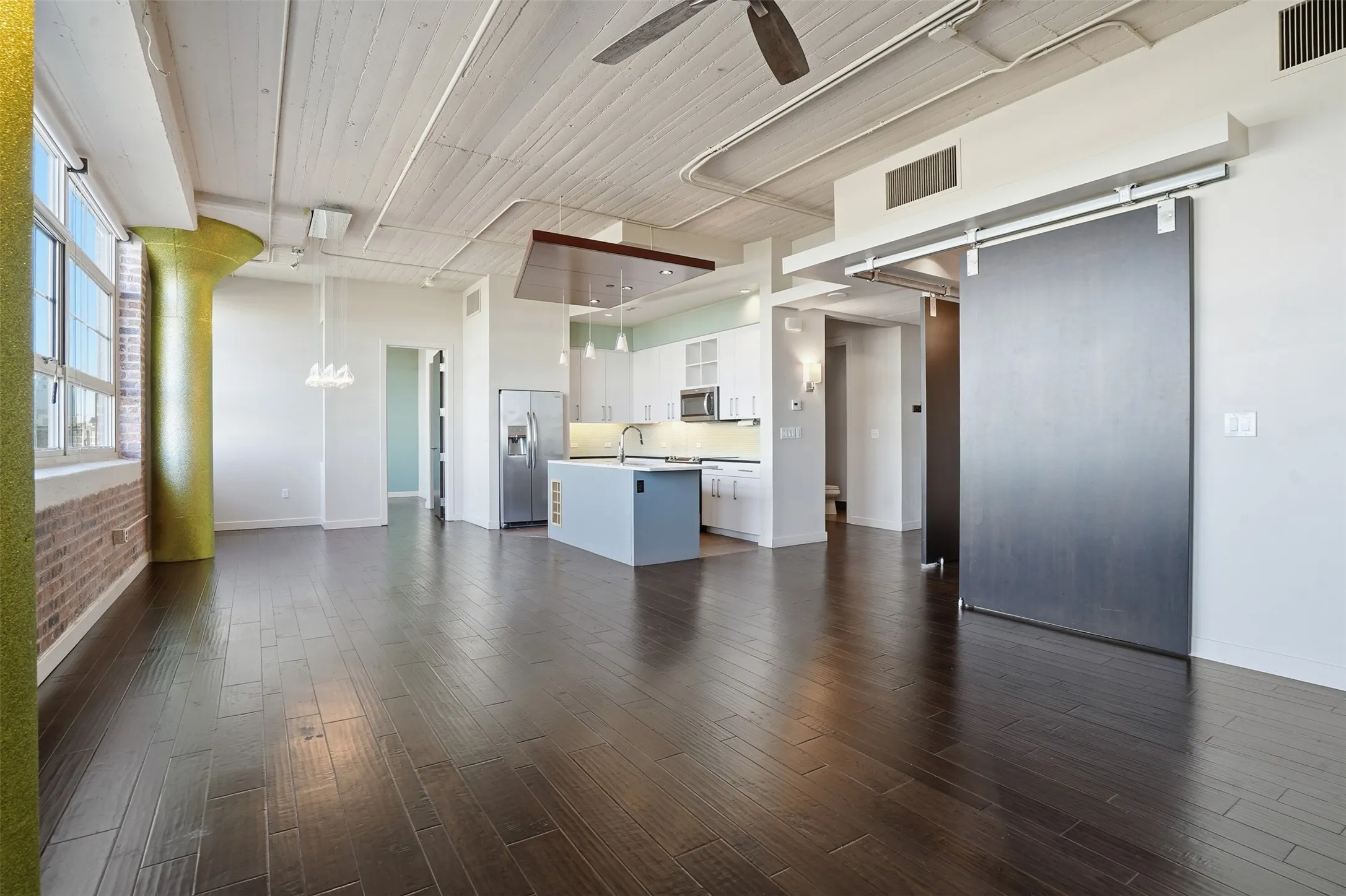 Open-concept living space featuring wood-finish flooring, exposed brick, and a modern kitchen