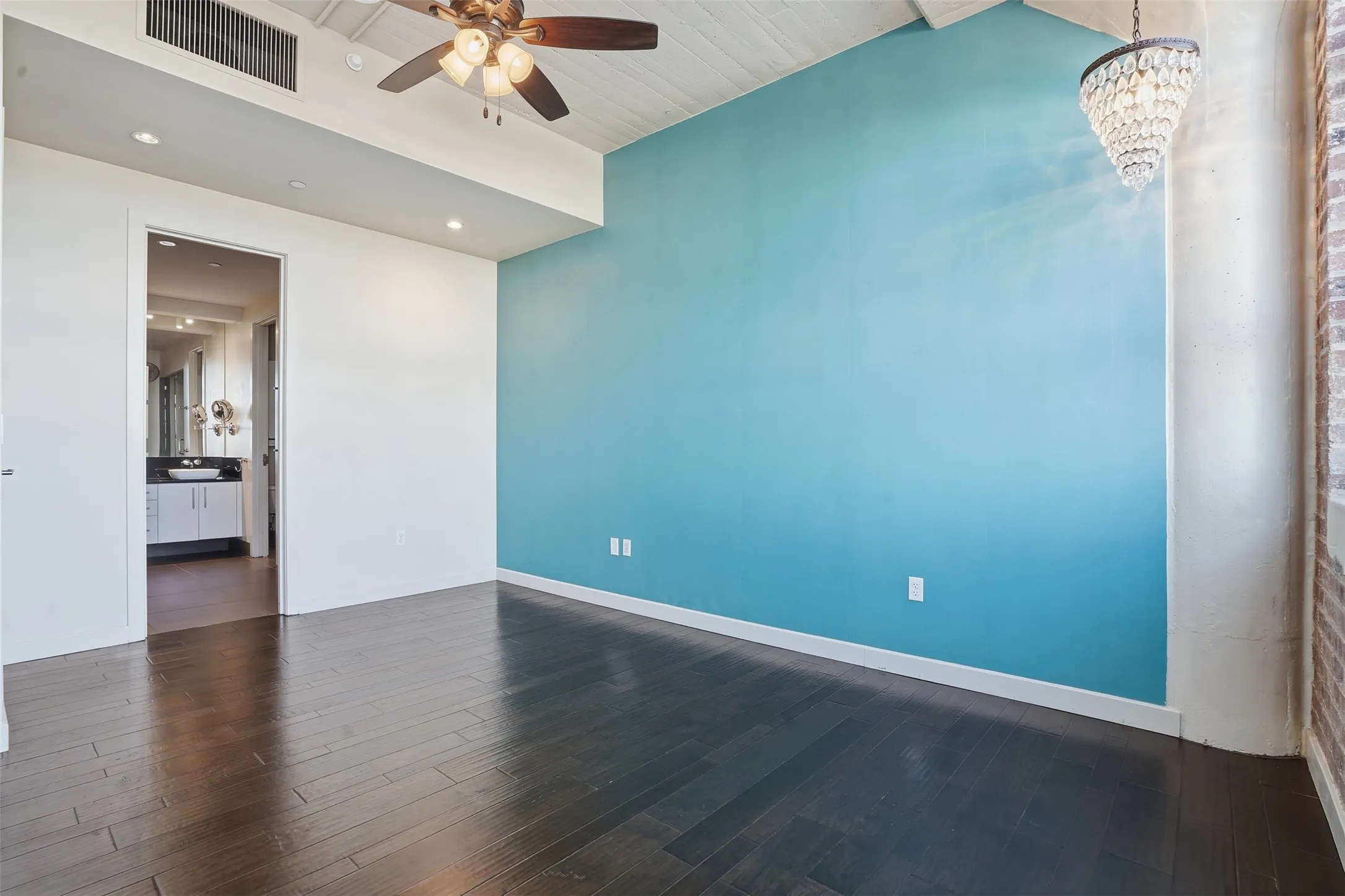 Spacious room with dark wood-finish flooring, a vibrant accent wall, and an exposed brick architectural detail