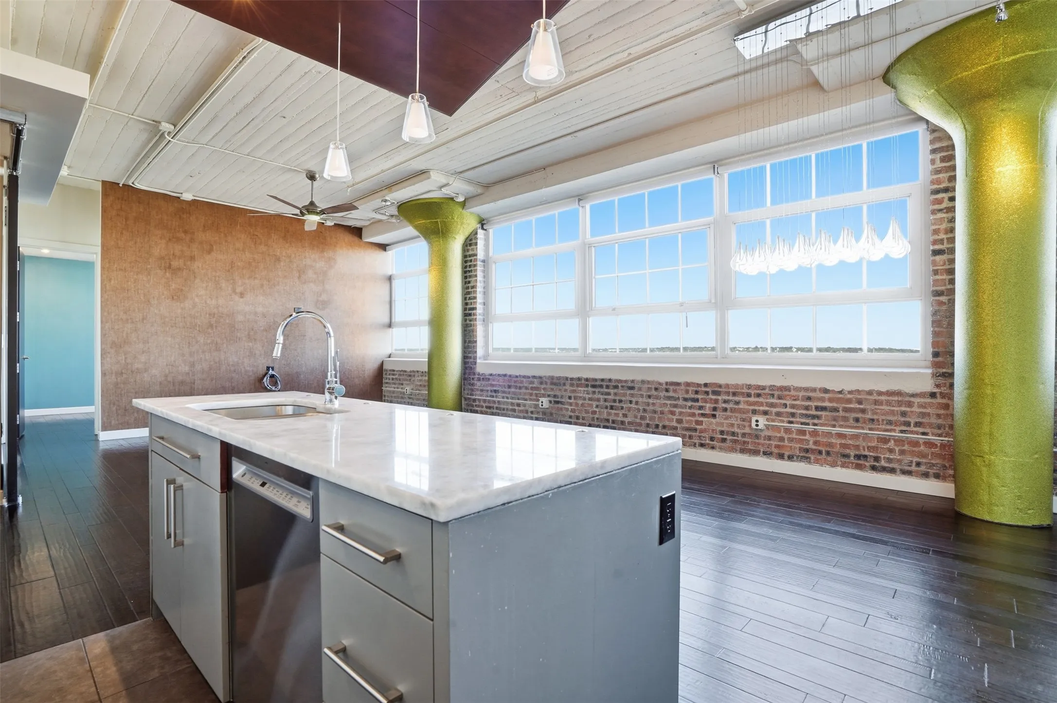 Expansive windows with multiple panes, exposed brick wall, wood-finish flooring, and a kitchen island with a built-in sink and dishwasher