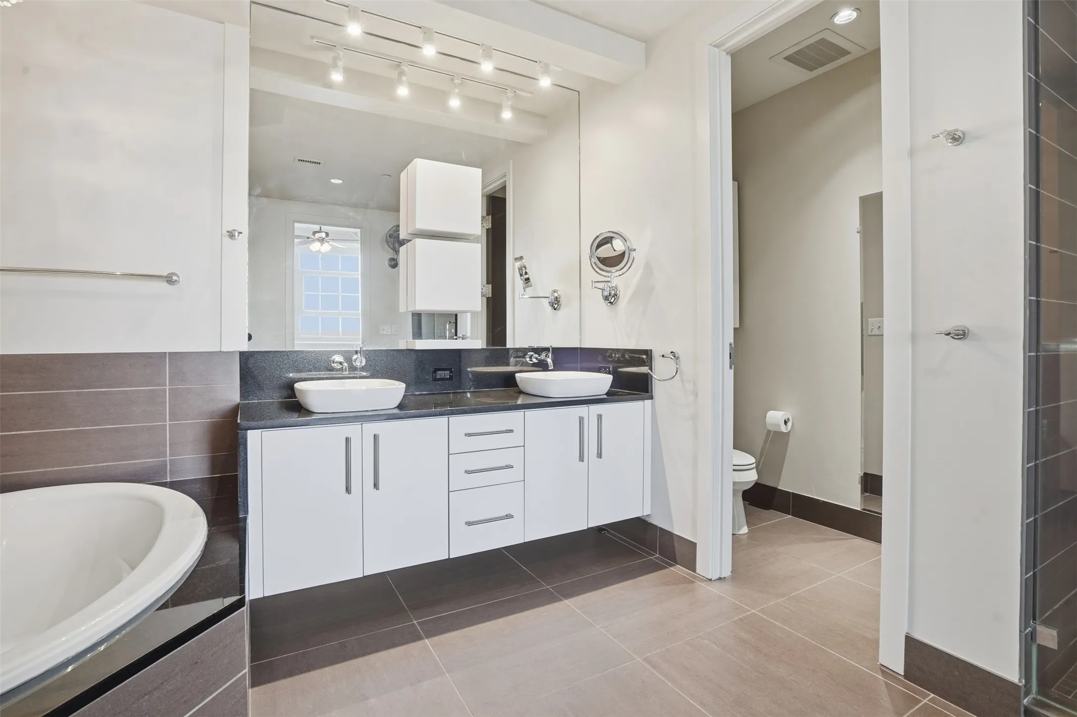 Dual vessel sinks set on a black countertop, white base cabinetry with brushed nickel hardware, and an expansive wall-mounted mirror