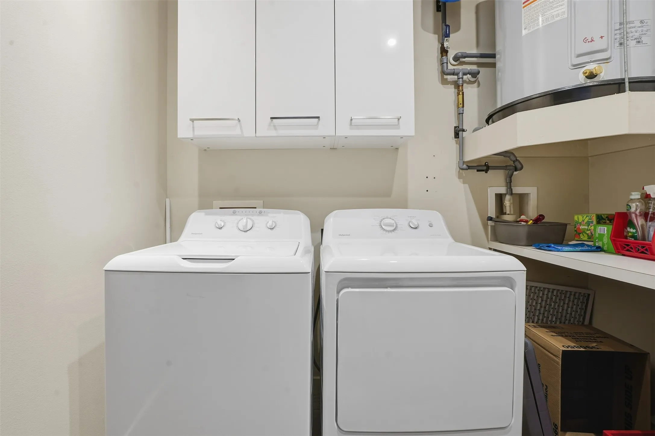 Laundry area featuring a top-load washer, a front-load dryer, upper white cabinetry with silver pulls, a built-in shelf, and a water heater