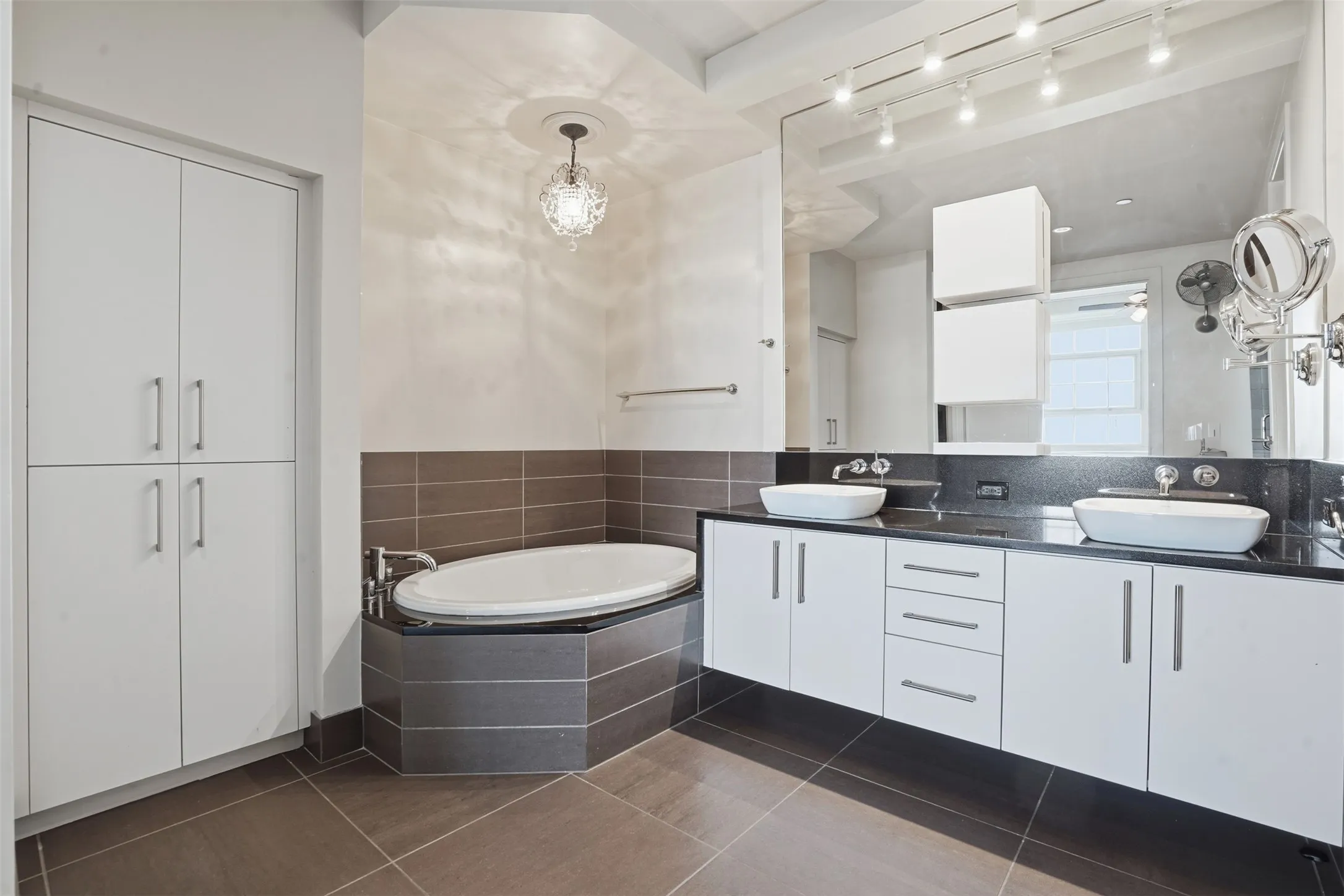 Contemporary bathroom featuring a built-in soaking tub, dual vessel sinks, a wide vanity with ample storage, a full-height mirror, and overhead track lighting