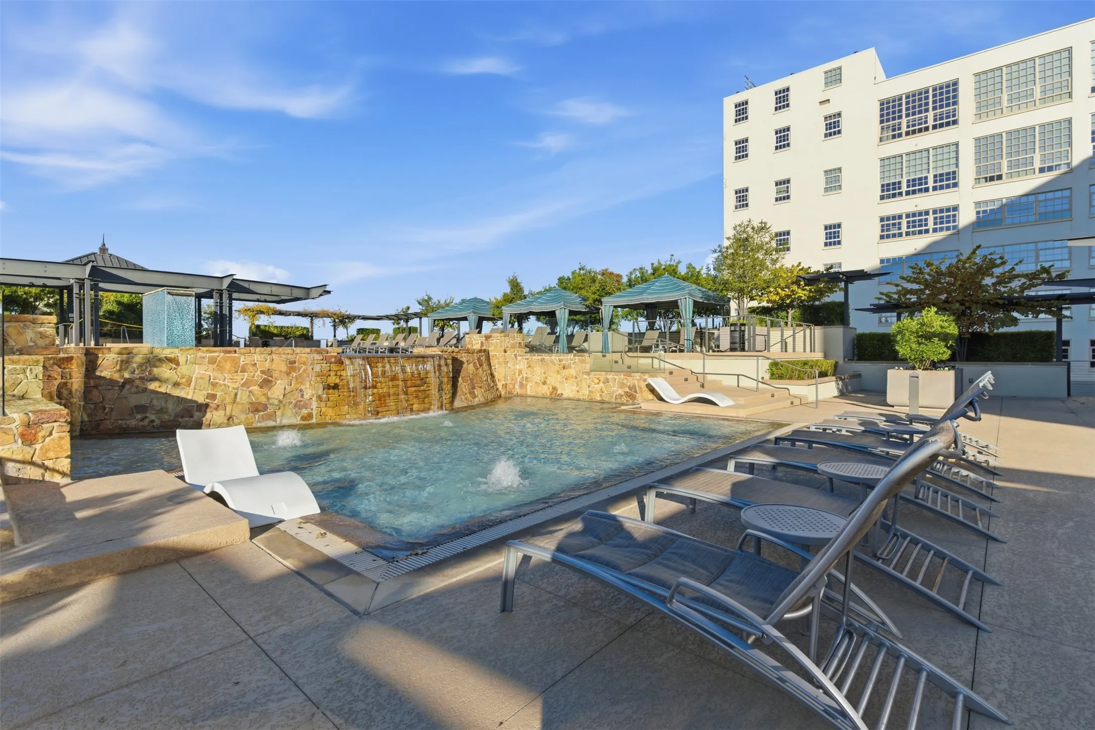 Outdoor pool featuring a stone-clad waterfall, integrated fountains, and a tile surround