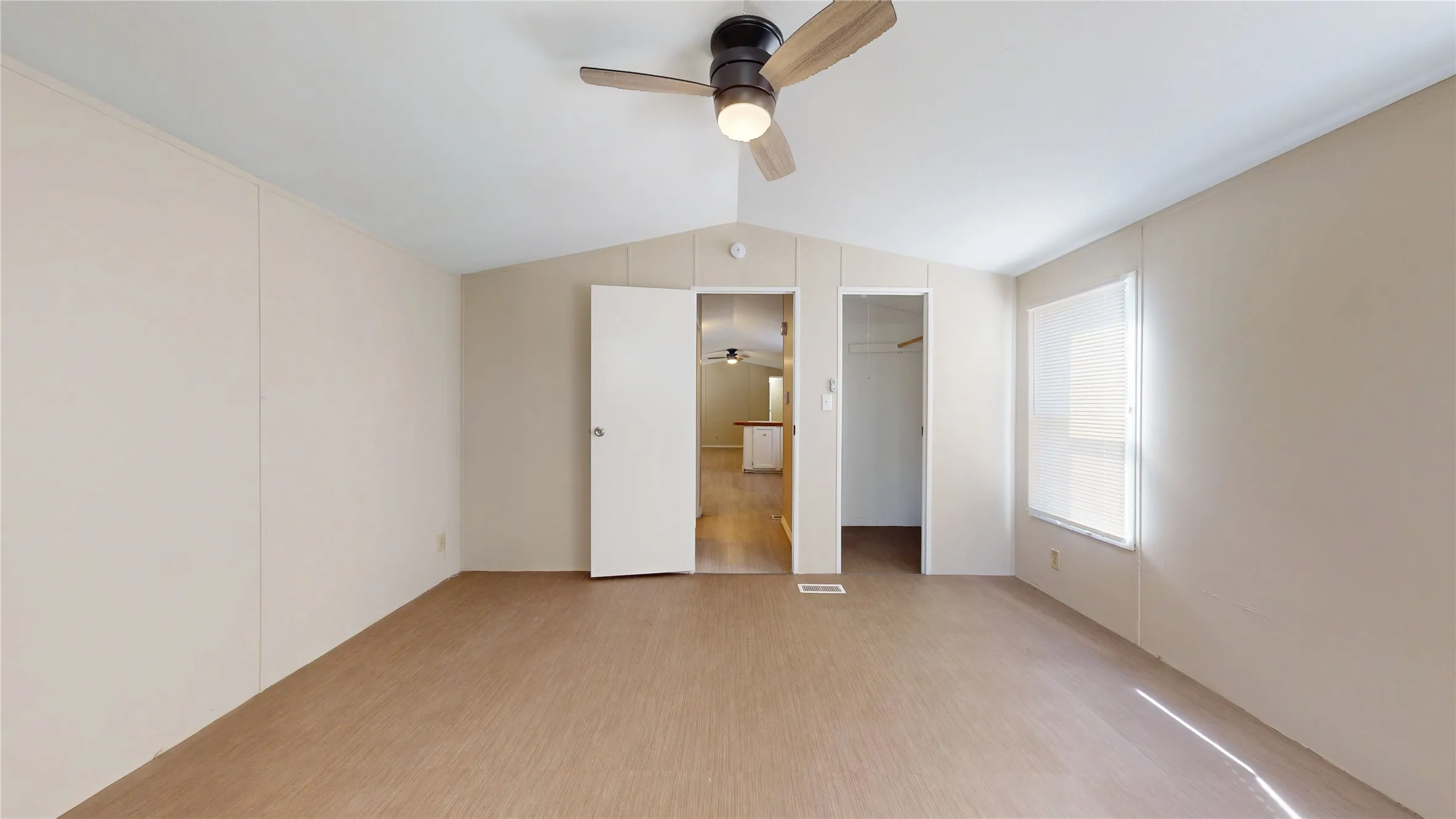Vaulted ceiling with a ceiling fan and light fixture, a window with a roller shade, light-toned walls, and wood-finish flooring
