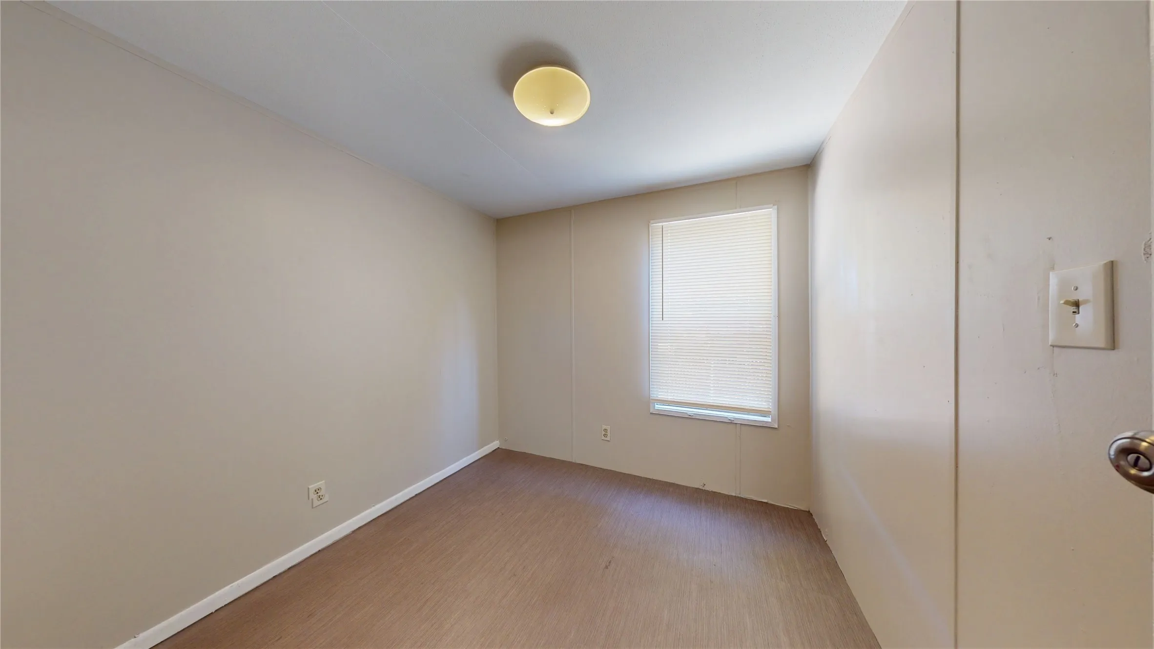 Wood-finish flooring with neutral wall paint, a single window, and flush-mount ceiling lighting