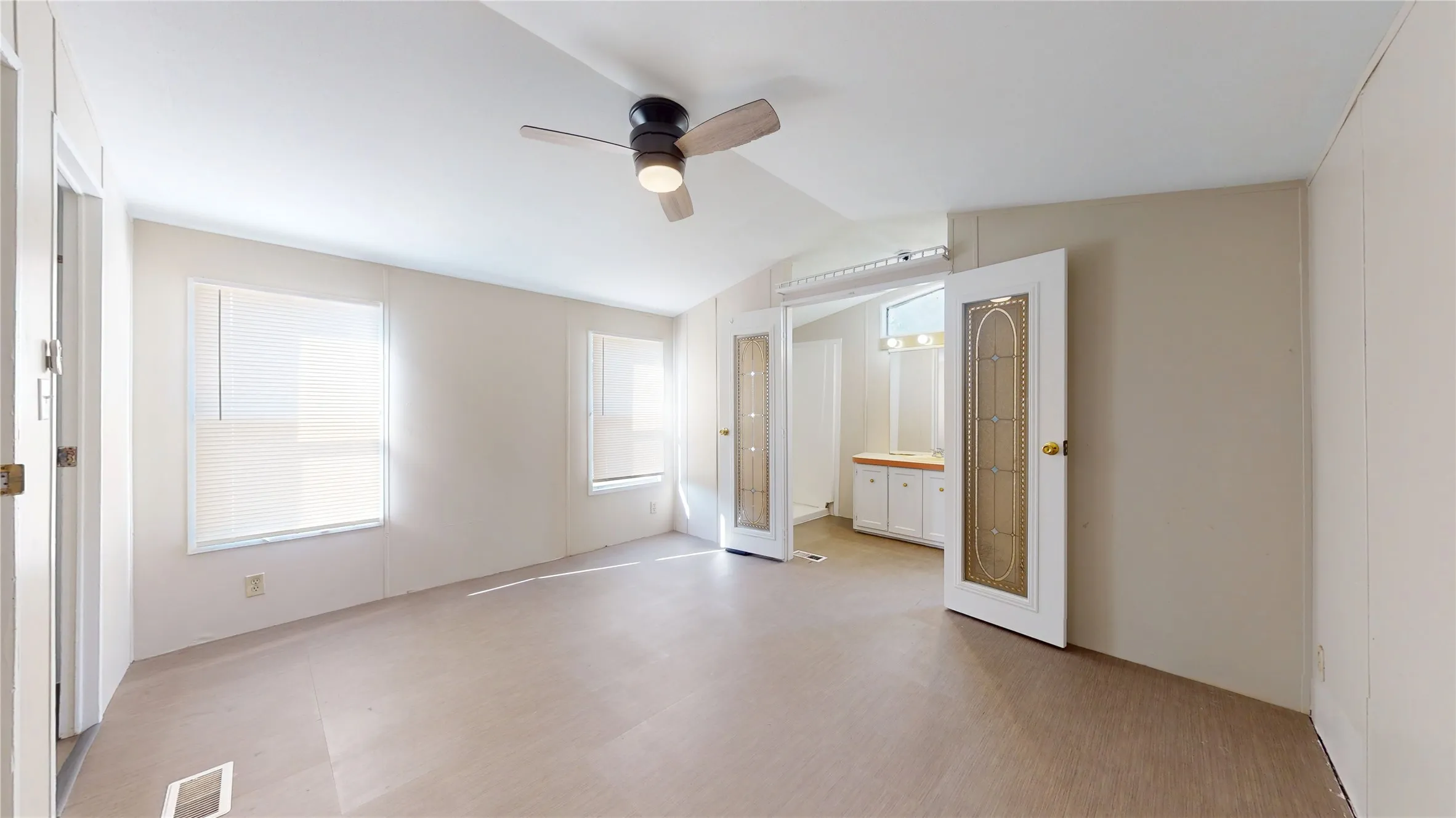 Wood-finish flooring, ceiling fan with integrated lighting, multiple windows, double-door entry with decorative glass panels, built-in vanity with white cabinetry