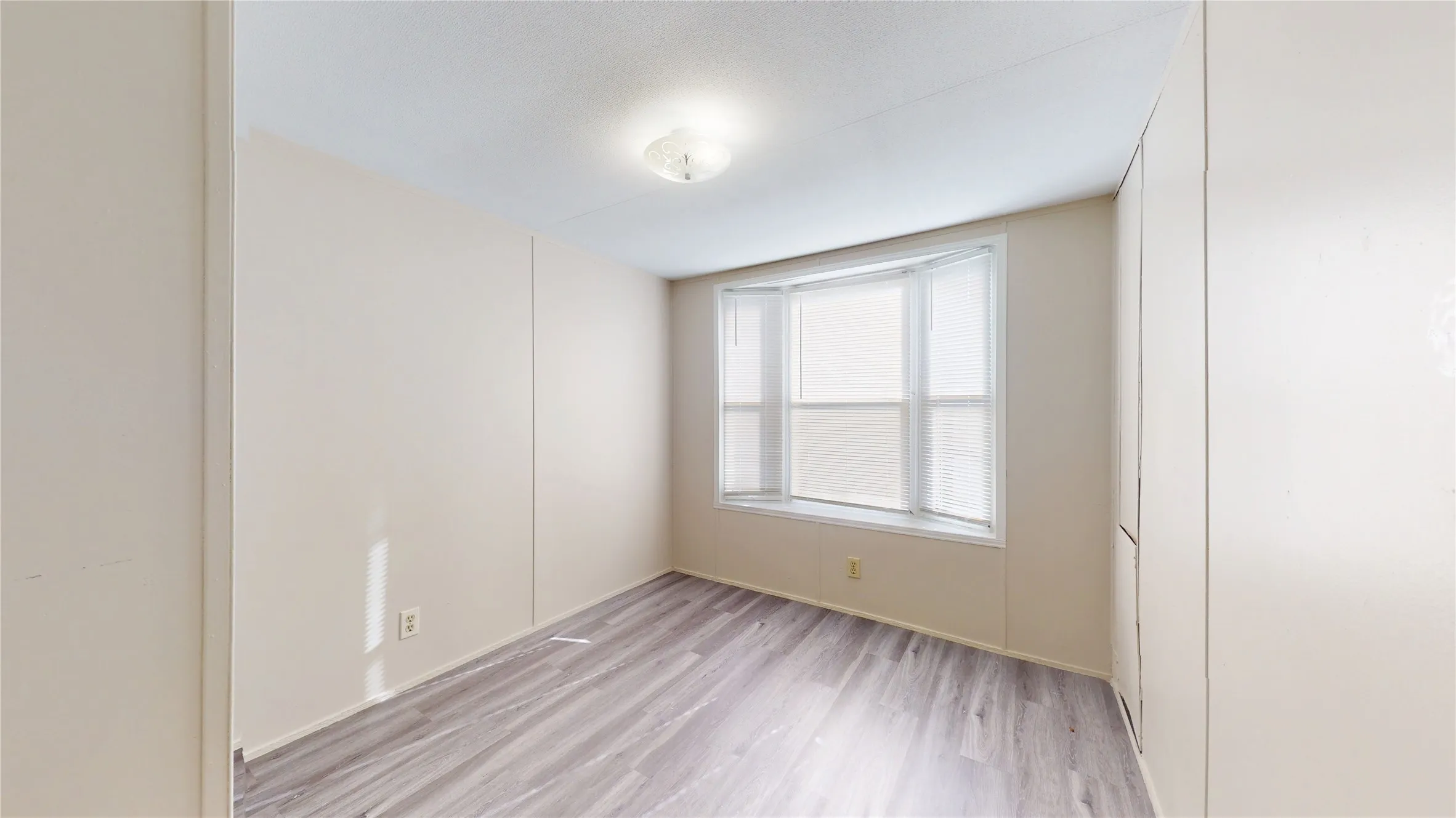 Bay window with blinds, wood-finish flooring, and a flush mount ceiling light