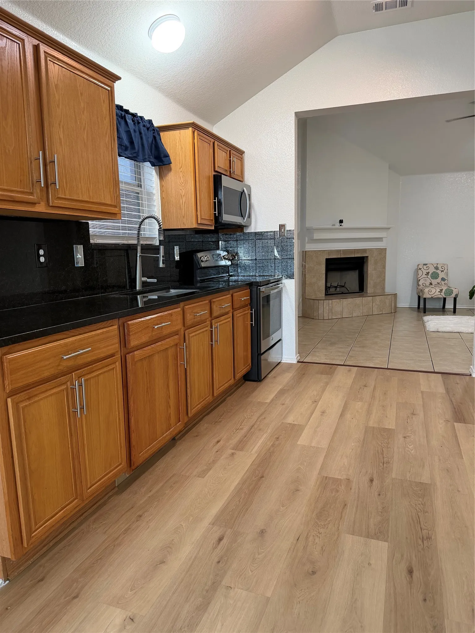 Kitchen with wood-finish flooring, wood cabinetry, dark countertops, and stainless steel appliances
