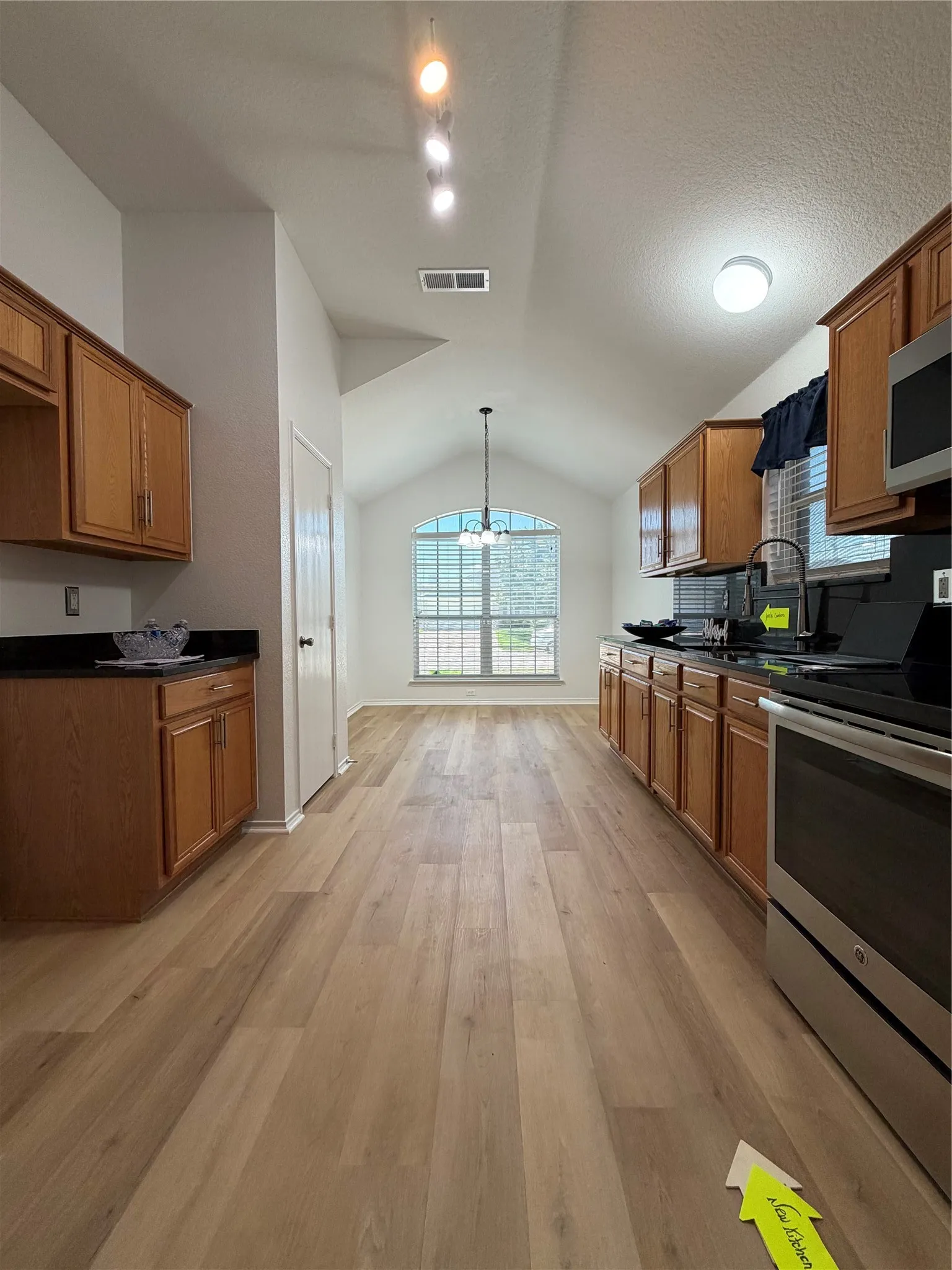 Open-concept kitchen and dining area featuring wood-finish flooring, vaulted ceilings, and an arched window