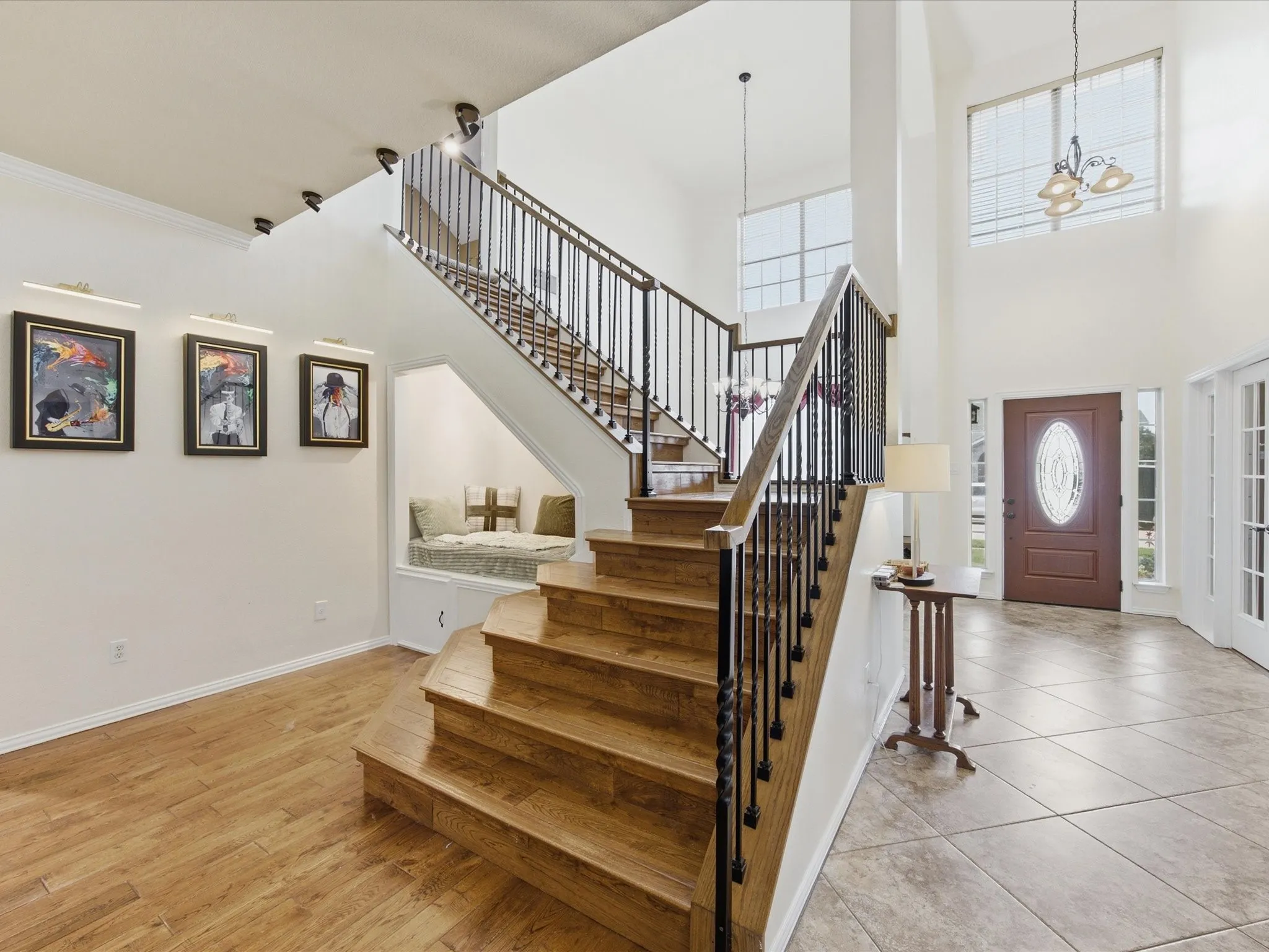 Two-story foyer featuring wood-finish flooring, a grand staircase with wrought iron balusters, a built-in window seat, a decorative front door with an oval glass insert, and high ceilings with upper-level windows