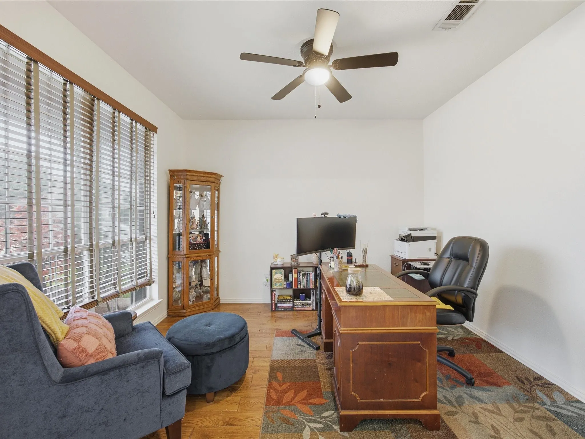 Spacious room featuring wood-finish flooring, a ceiling fan with integrated lighting, and multiple windows with horizontal blinds