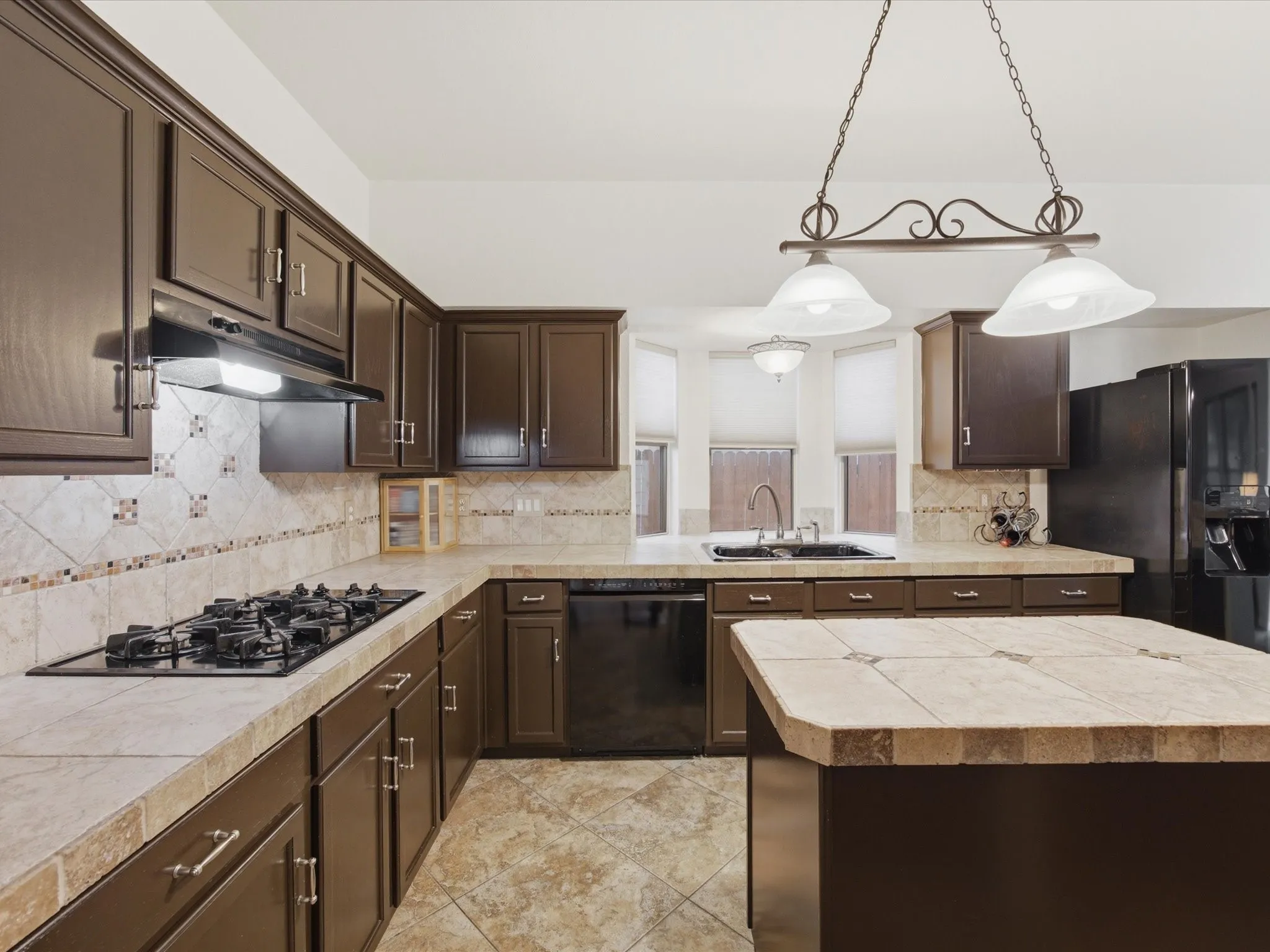 Kitchen featuring dark wood-finish cabinetry, tile countertops, a gas cooktop, and a matching tile​​‌​​​​‌​​‌‌​‌‌​​​‌‌​‌​‌​‌​​​‌​​ backsplash