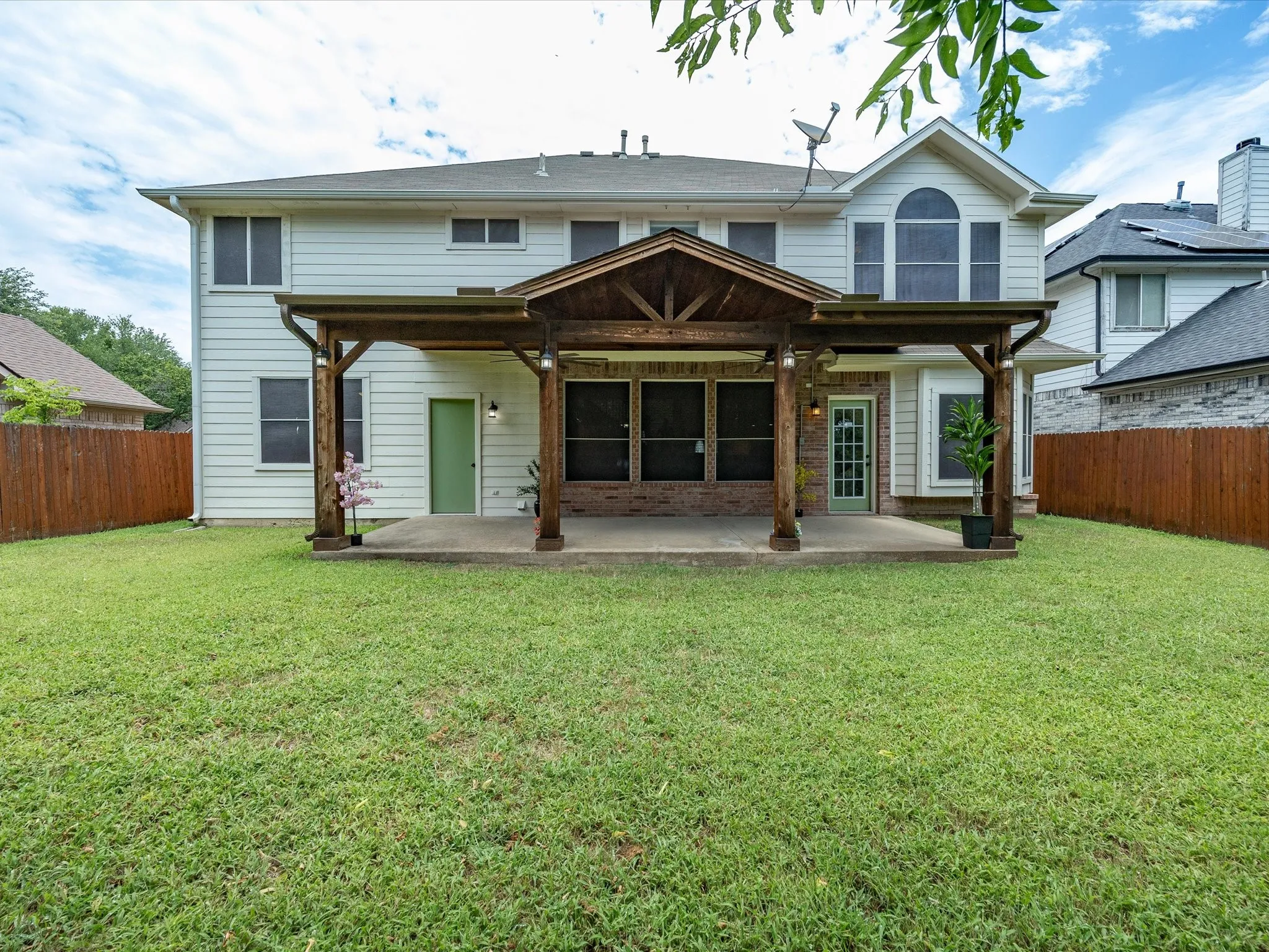 Spacious backyard featuring a covered patio with exposed wood beams, concrete slab, and brick accents