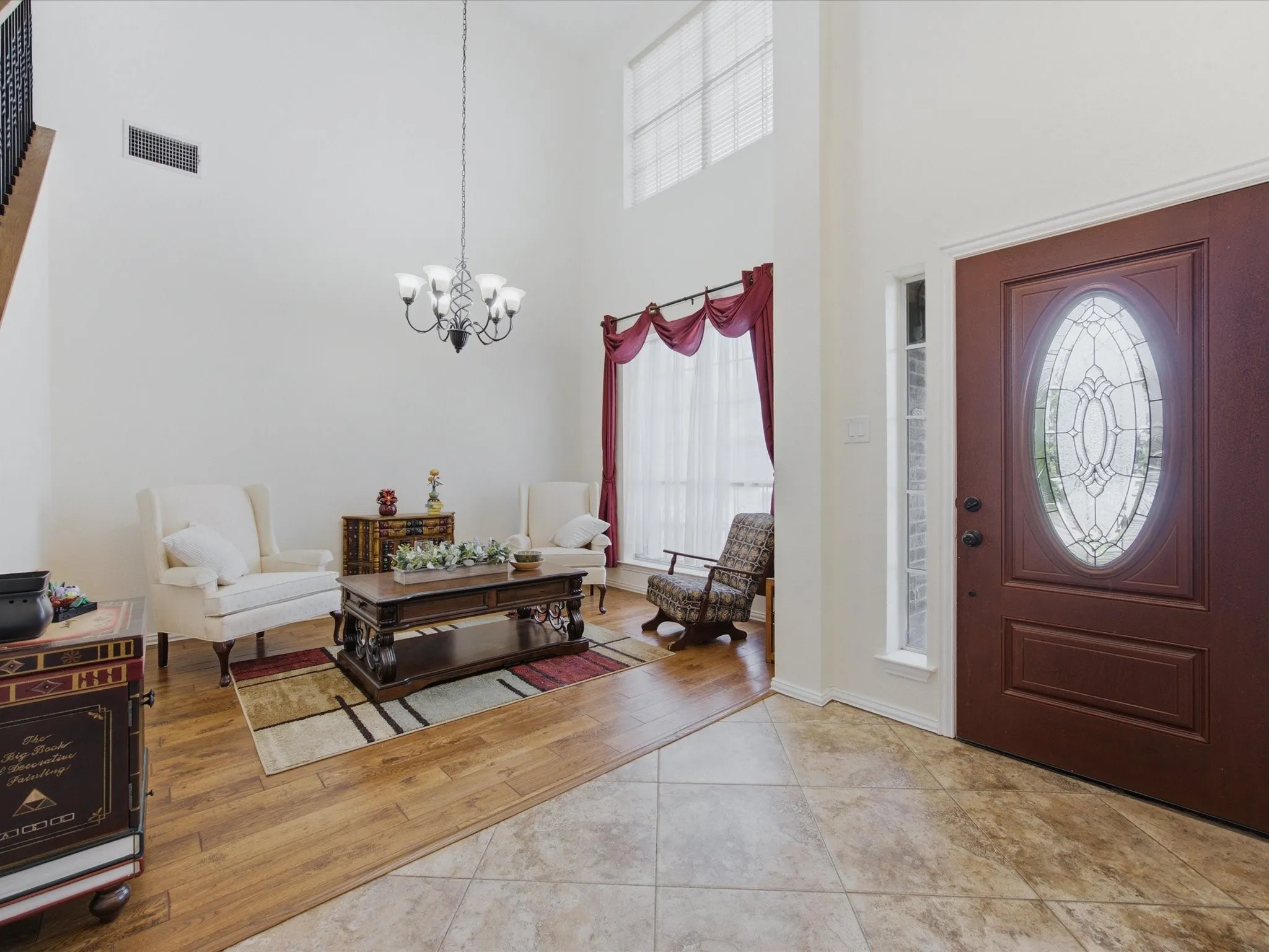 Two-story foyer featuring a decorative glass panel front door, high ceilings, a wrought iron chandelier, wood-finish flooring, and a staircase with an open railing