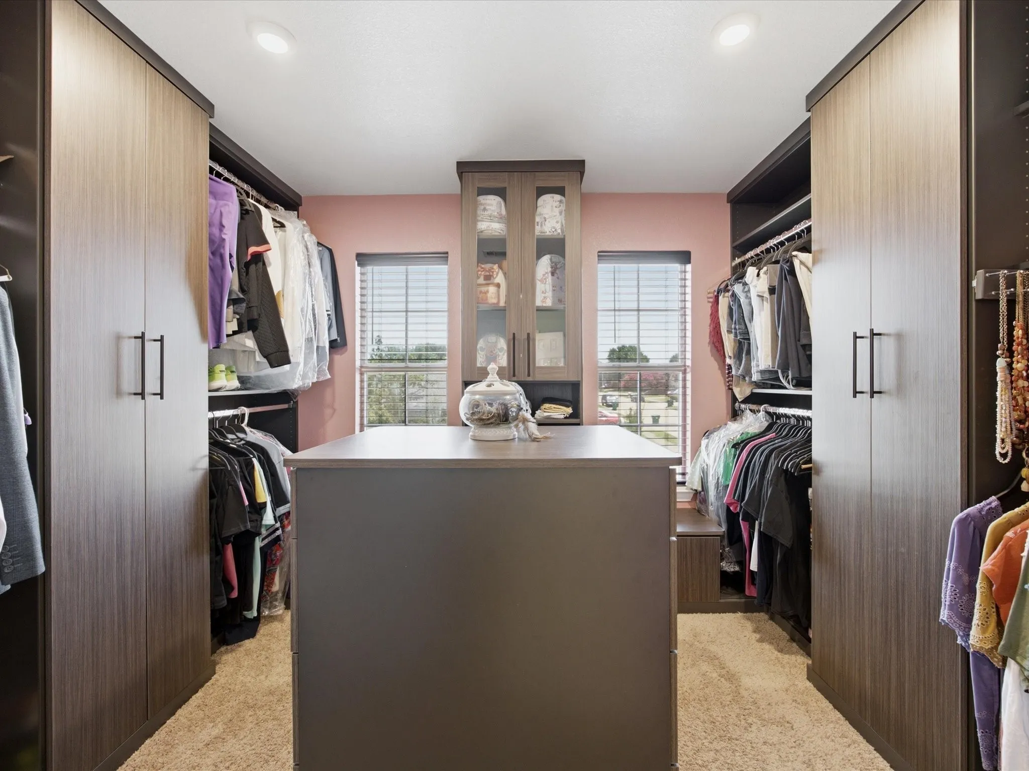 Custom closet organization system featuring a central island, built-in cabinetry with glass inserts, and wood-finish wardrobe doors
