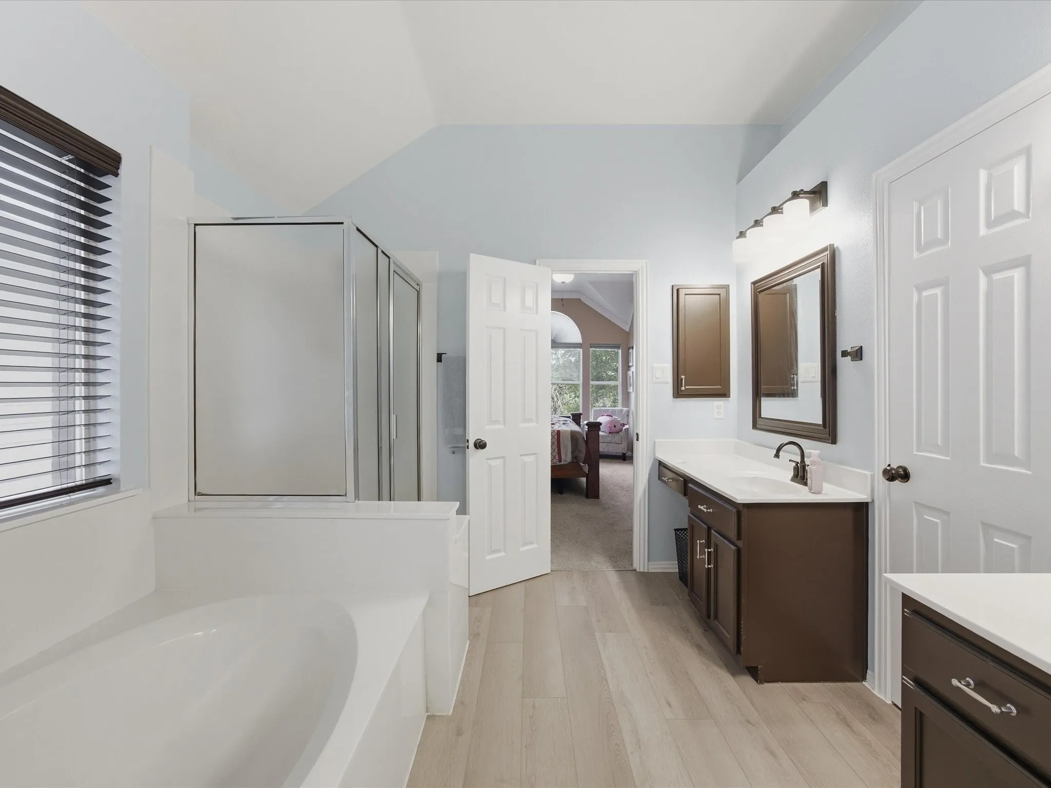 Primary Bathroom featuring wood-finish flooring, a built-in soaking tub, a stand-up shower with a glass enclosure, and a vanity with a white countertop