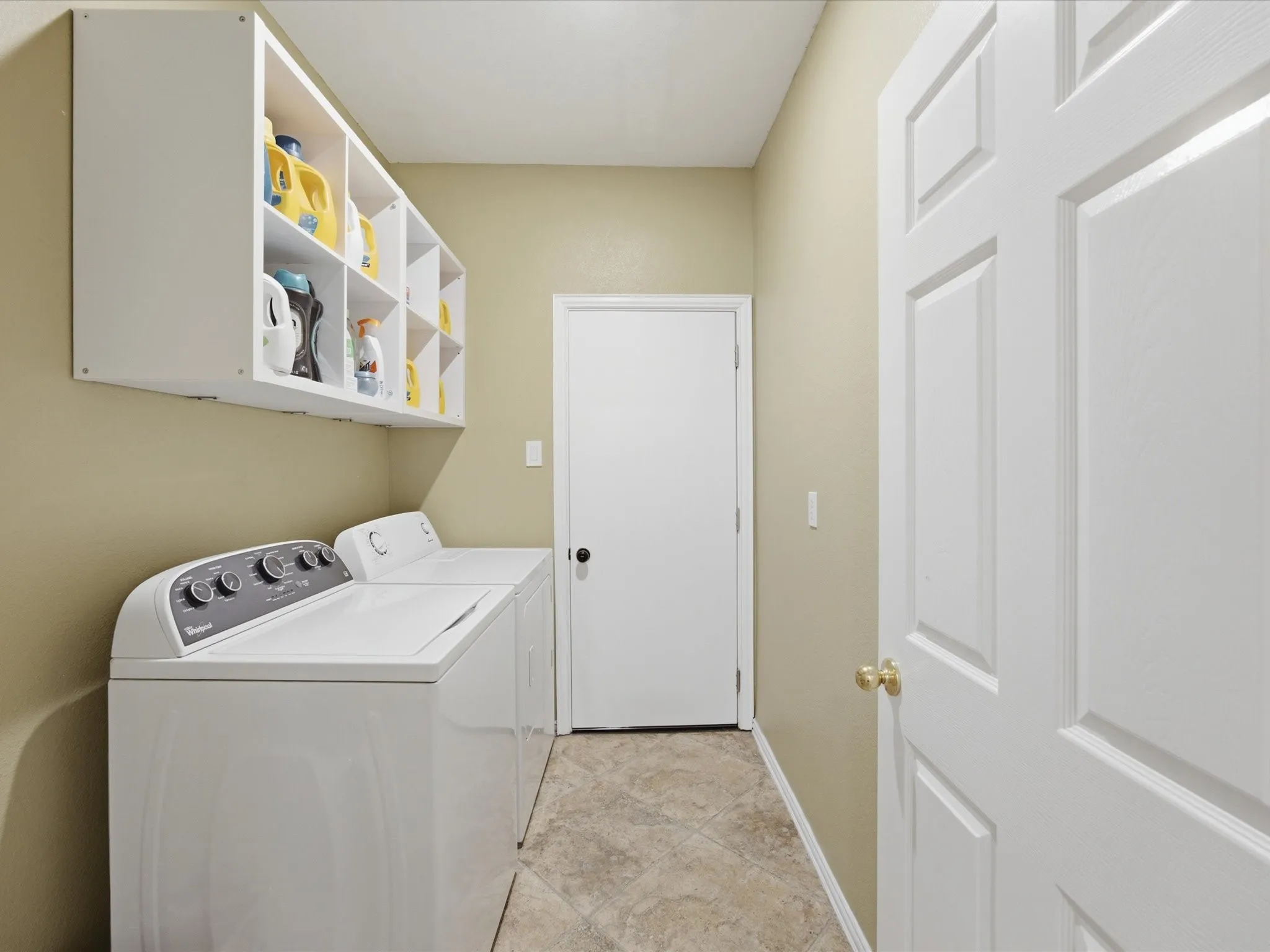 Dedicated laundry area featuring a top-load washing machine and dryer, overhead white storage cubbies, neutral wall paint, and patterned floor tiles