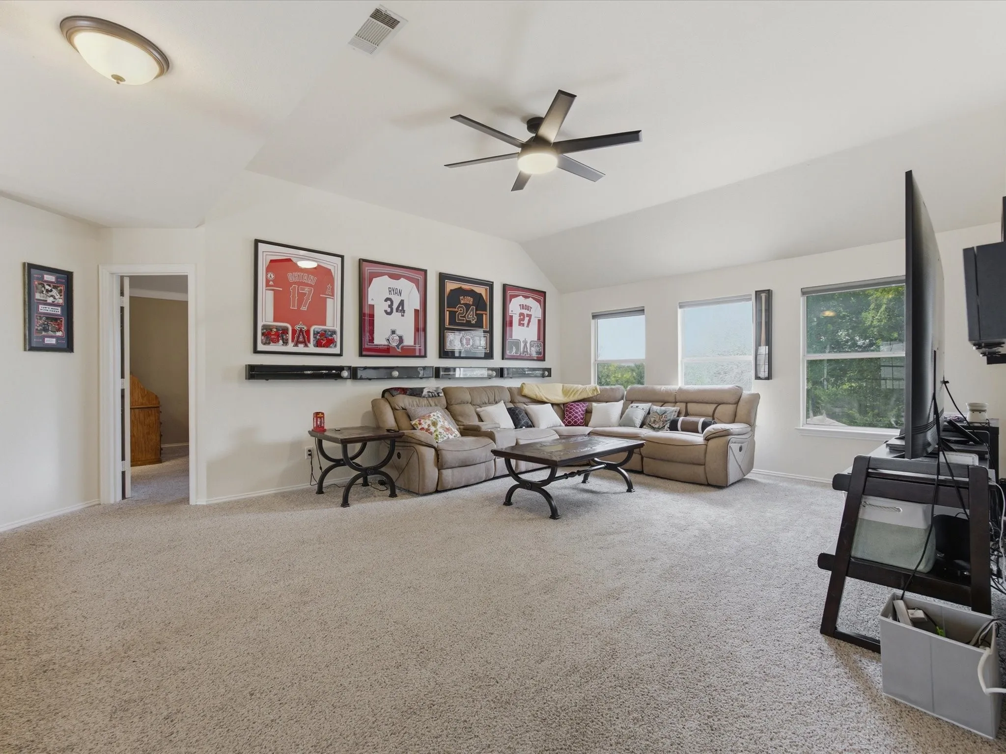 Spacious bonus room featuring vaulted ceilings, a ceiling fan with integrated lighting, recessed windows with roller shades, and light-toned carpeting