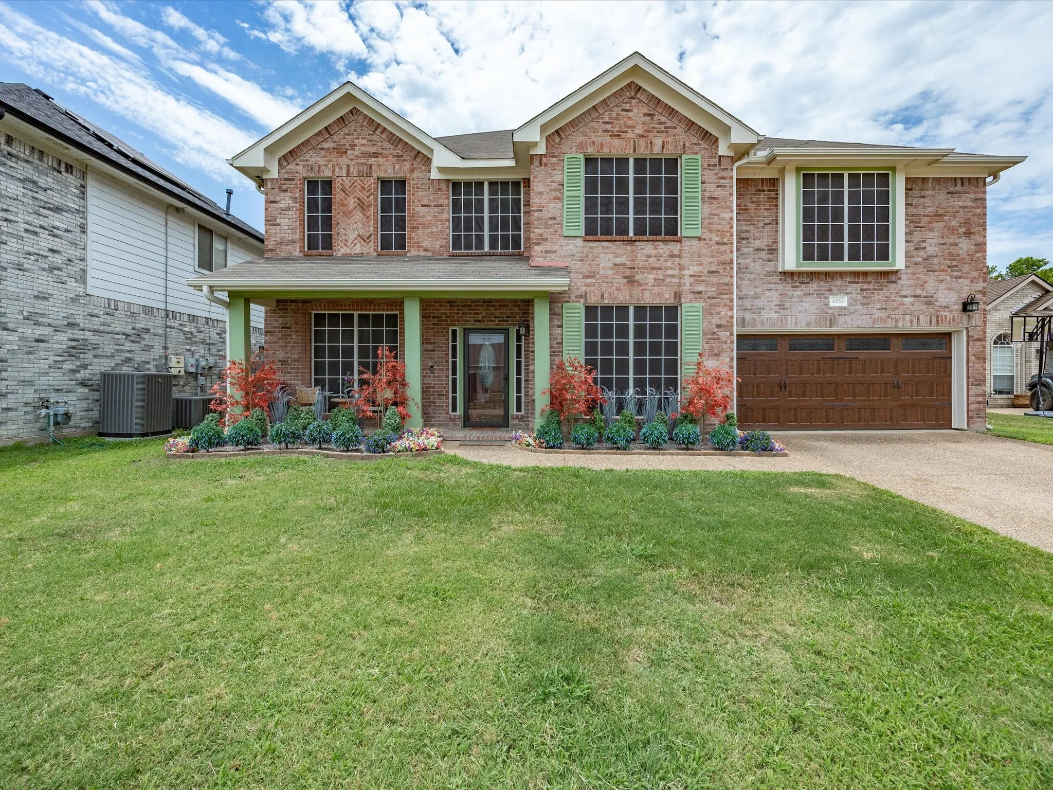 Two-story brick facade residence featuring a covered front porch with columns, a two-car garage with a wood-finish door, and prominent window screens