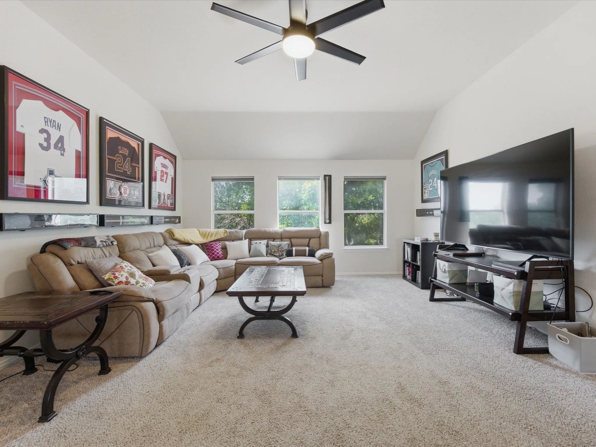 Spacious living area featuring wood-finish flooring, white baseboards, and a ceiling fan with integrated lighting