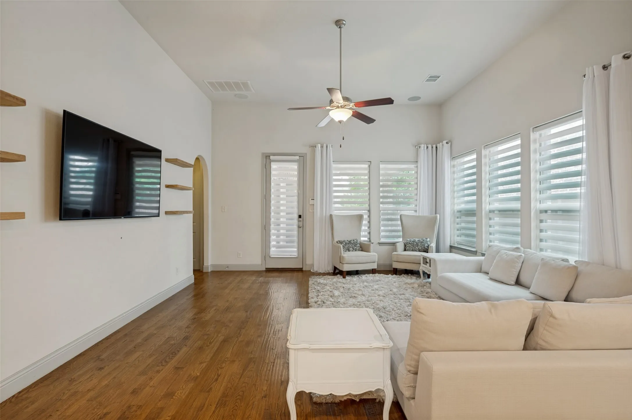 Spacious living area featuring wood-finish flooring, vaulted ceilings, and a ceiling fan with integrated lighting