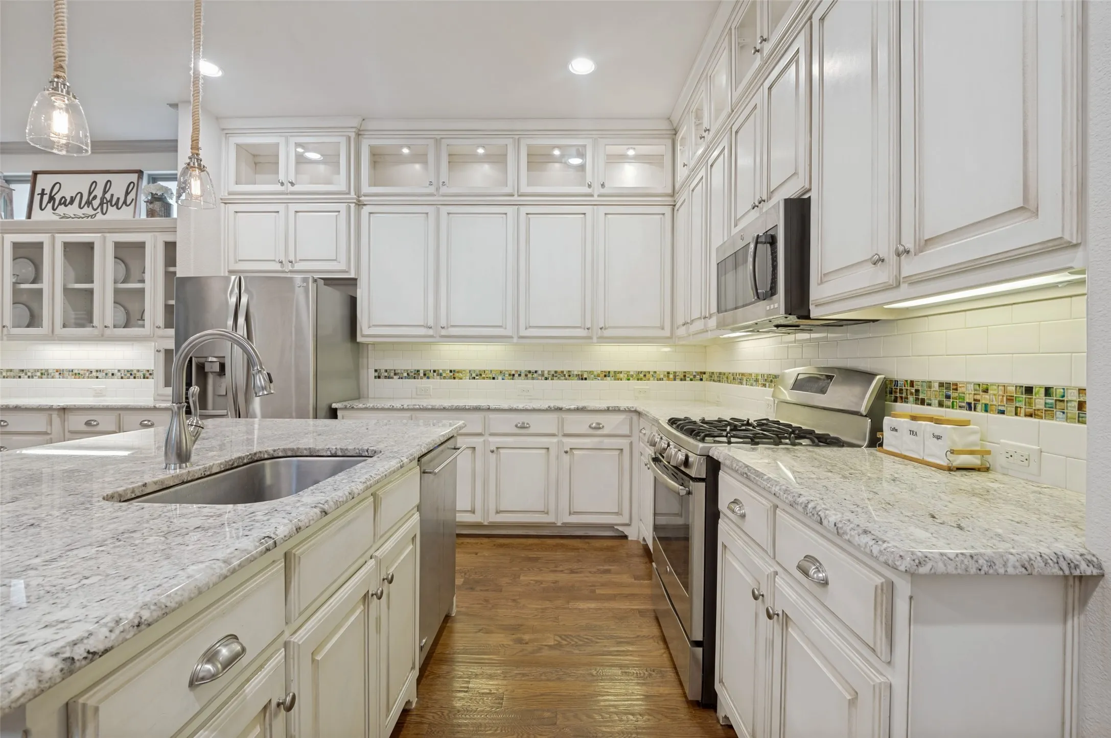Kitchen featuring white cabinetry, light-toned countertops, a stainless steel sink, and wood-finish flooring