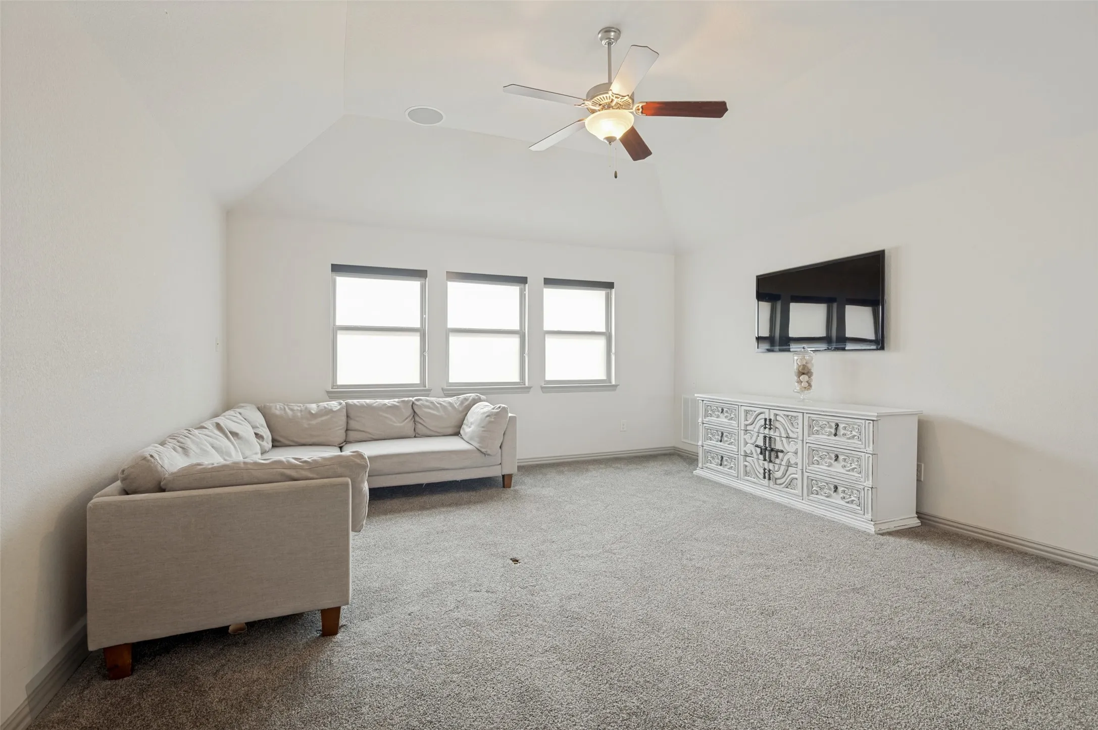 Carpeted room with a vaulted ceiling, ceiling fan with integrated lighting, recessed lighting, and a window bank