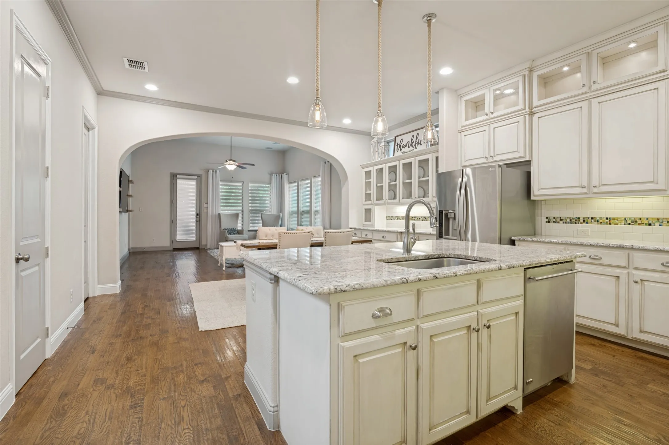 Open-concept kitchen featuring an island with a stainless steel sink, granite countertops, wood-finish flooring, white cabinetry, and stainless steel appliances