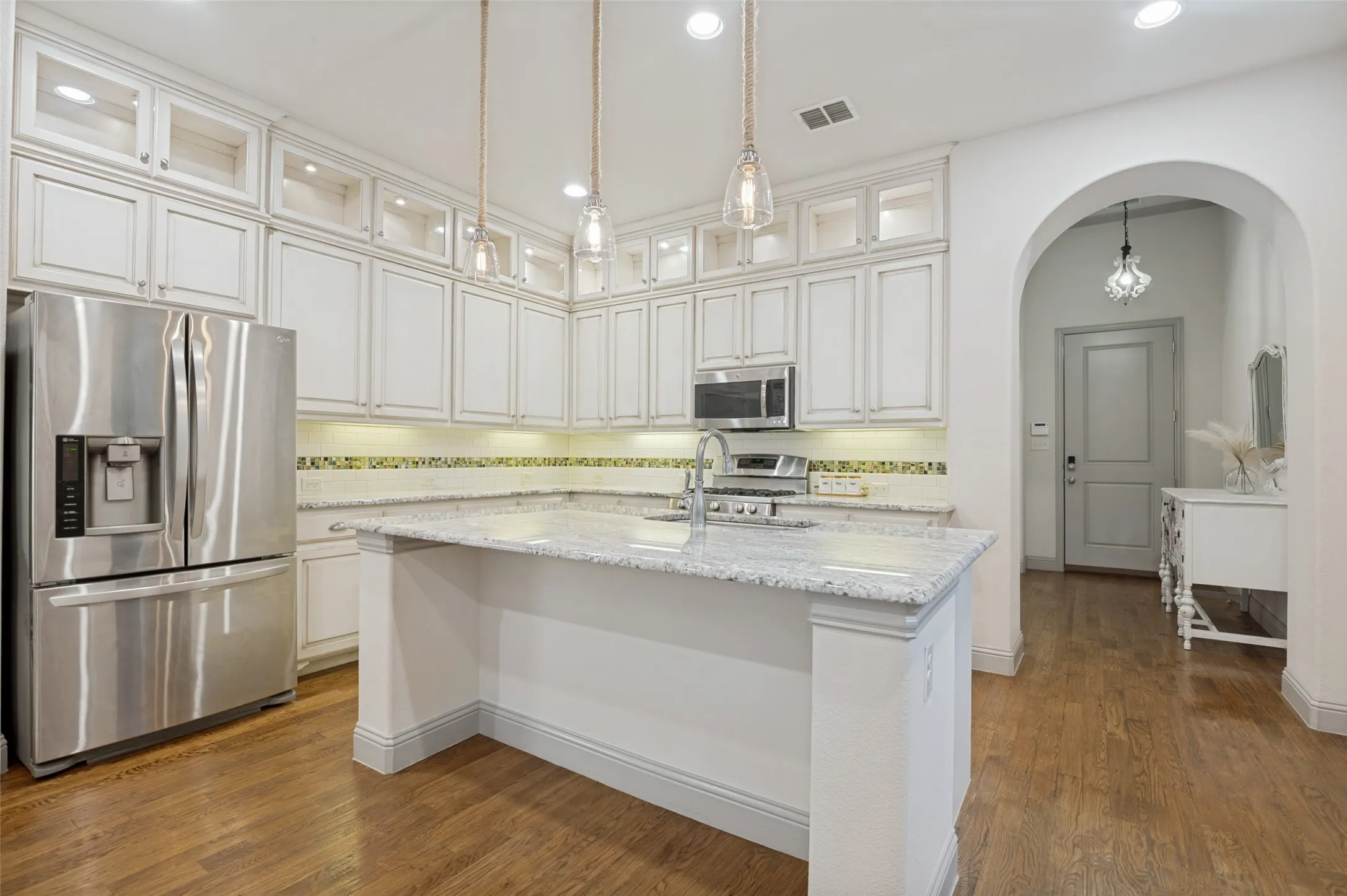 Kitchen featuring white cabinetry with glass-front uppers, stainless steel appliances, speckled stone countertops, and wood-finish flooring