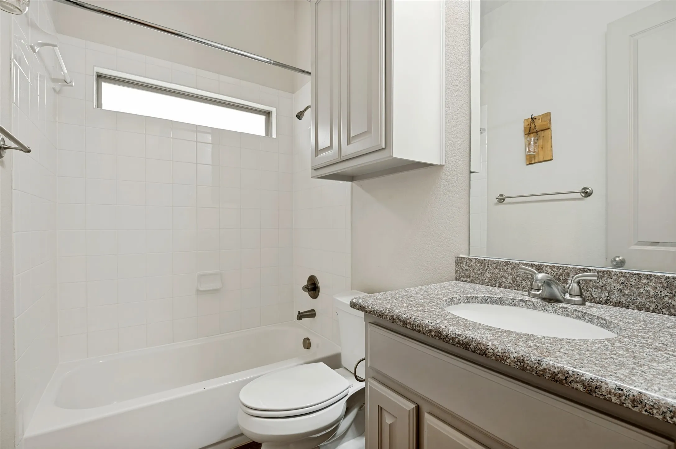 Bathroom featuring a tub/shower combination with white tile surround, a horizontal privacy window, and an overhead storage cabinet