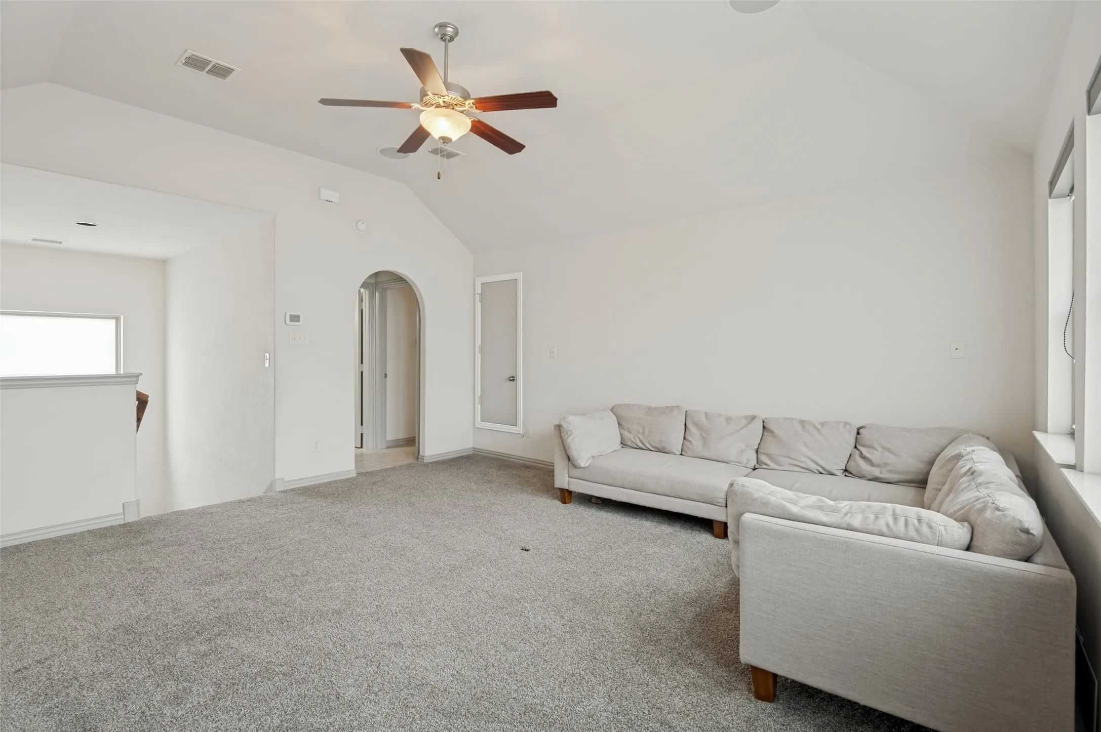 Expansive carpeted room featuring a vaulted ceiling and a ceiling fan with integrated lighting