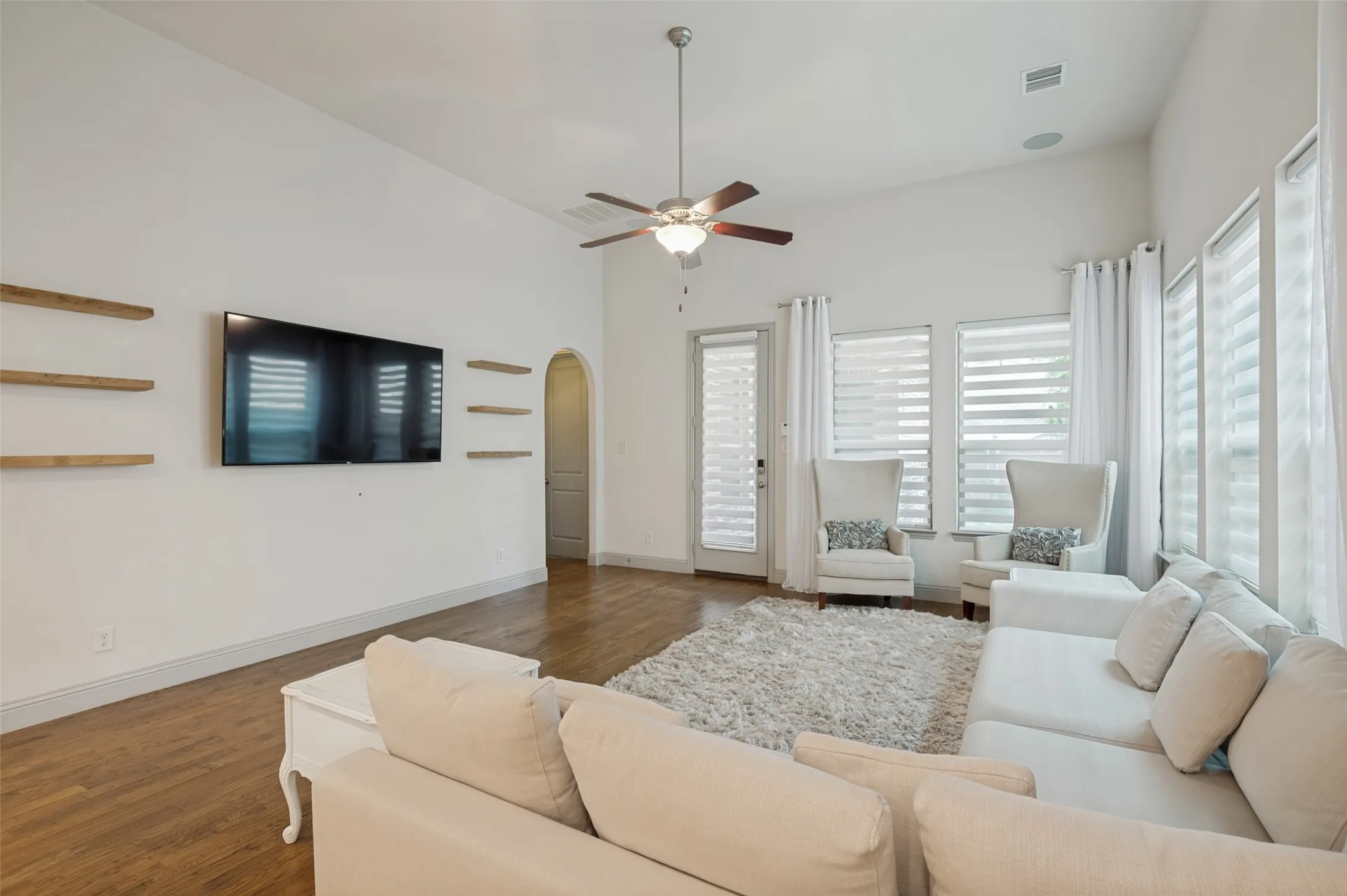 Living area featuring vaulted ceilings, wood-finish flooring, a ceiling fan, and multiple windows with blinds and drapes