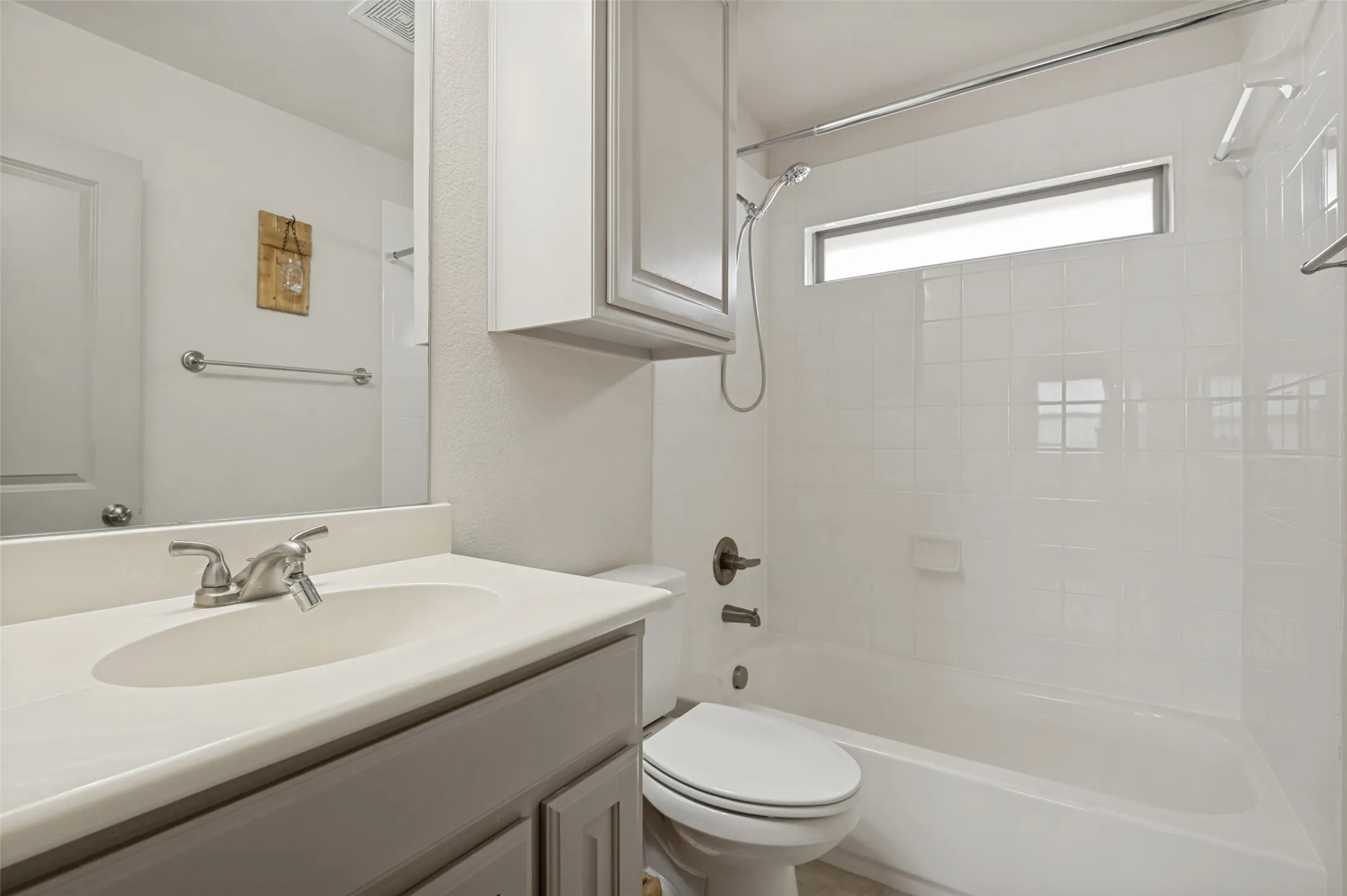Bathroom featuring a white subway tile shower surround, a built-in bathtub, a vanity with an integrated sink, and an upper storage cabinet