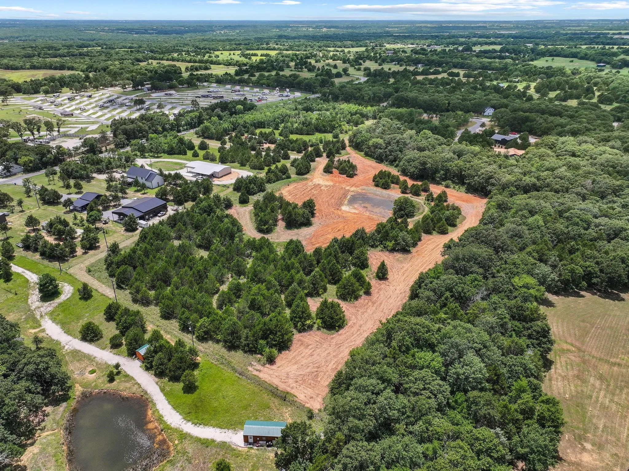 Expansive cleared land parcel surrounded by mature trees, featuring a distinct pond