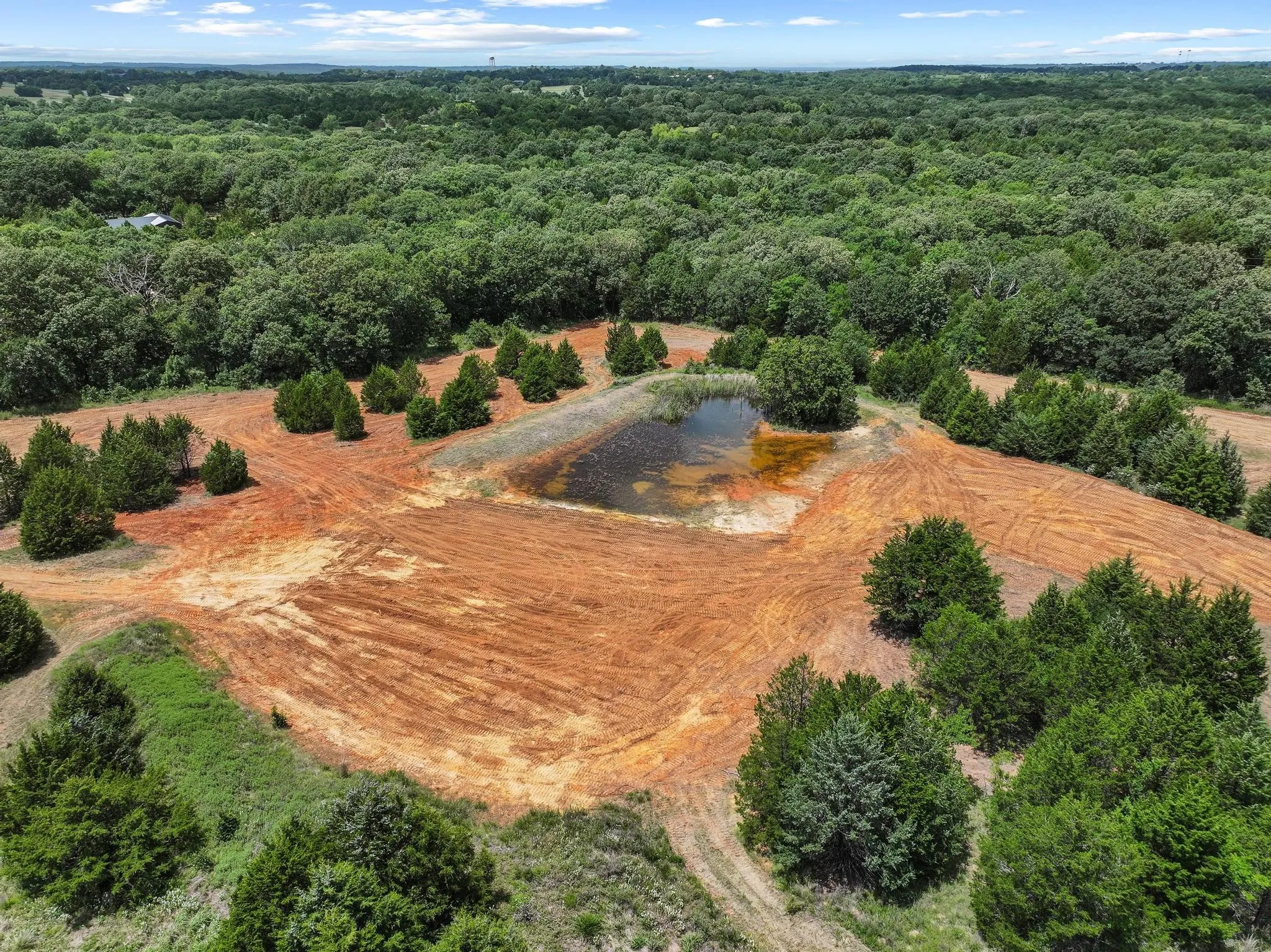 Expansive land parcel featuring a natural pond, partially cleared terrain, and mature trees